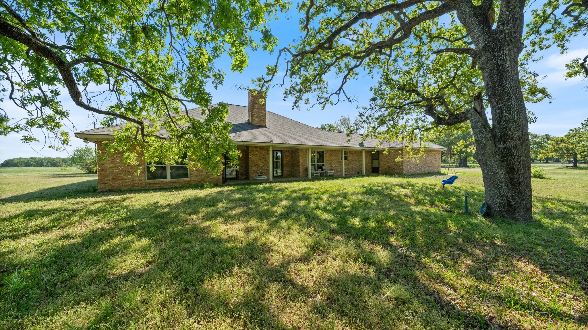 Rear view of house featuring a lawn, brick siding, a patio, and a chimney