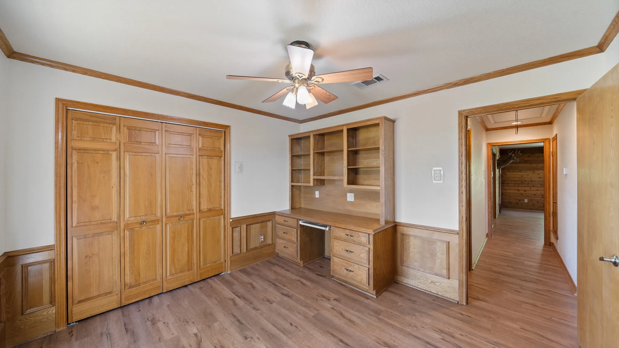 Unfurnished bedroom featuring a wainscoted wall, crown molding, a ceiling fan, a decorative wall, and light wood-style floors