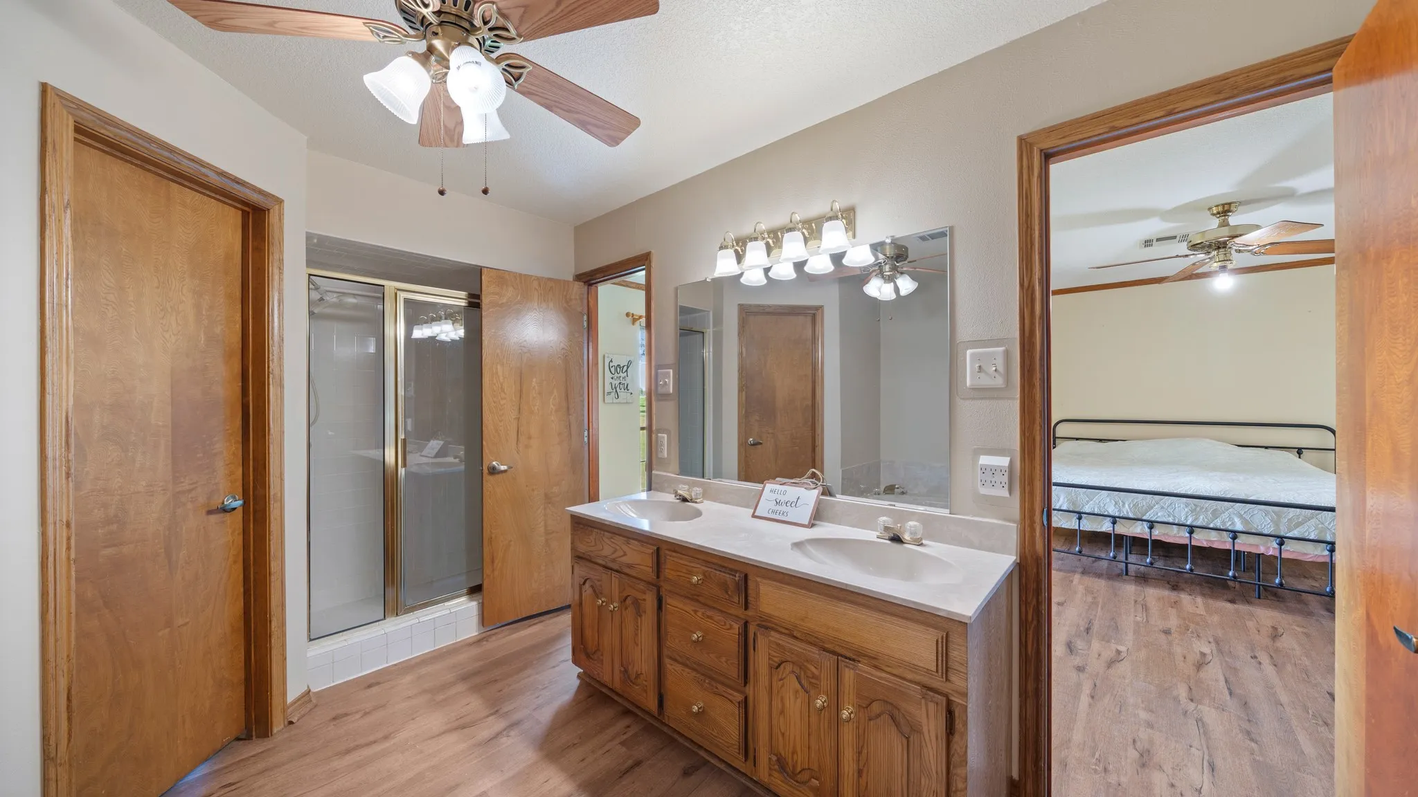 Ensuite bathroom with ceiling fan, double vanity, light wood-type flooring, and a stall shower