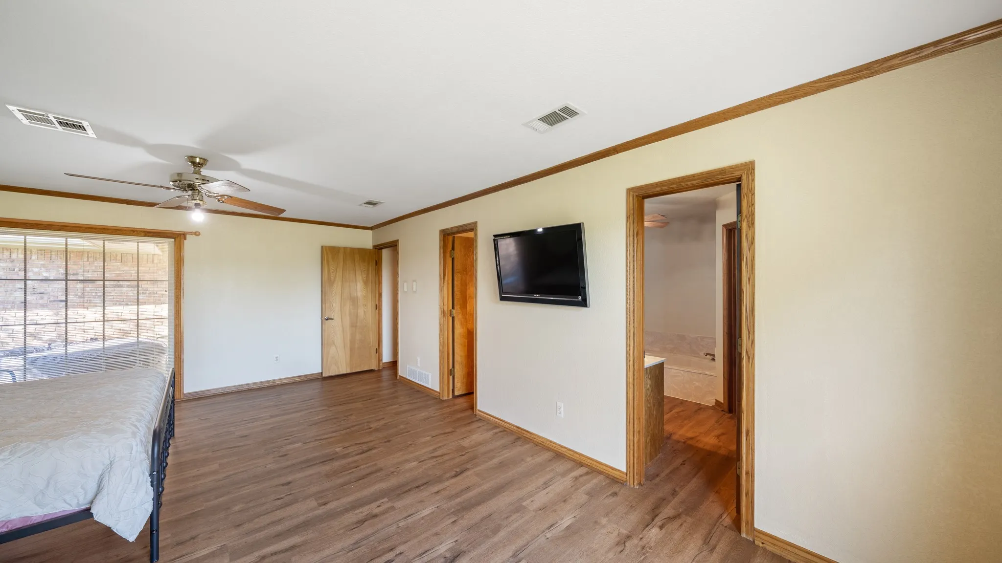 Unfurnished bedroom featuring crown molding, dark wood-type flooring, a ceiling fan, and connected bathroom