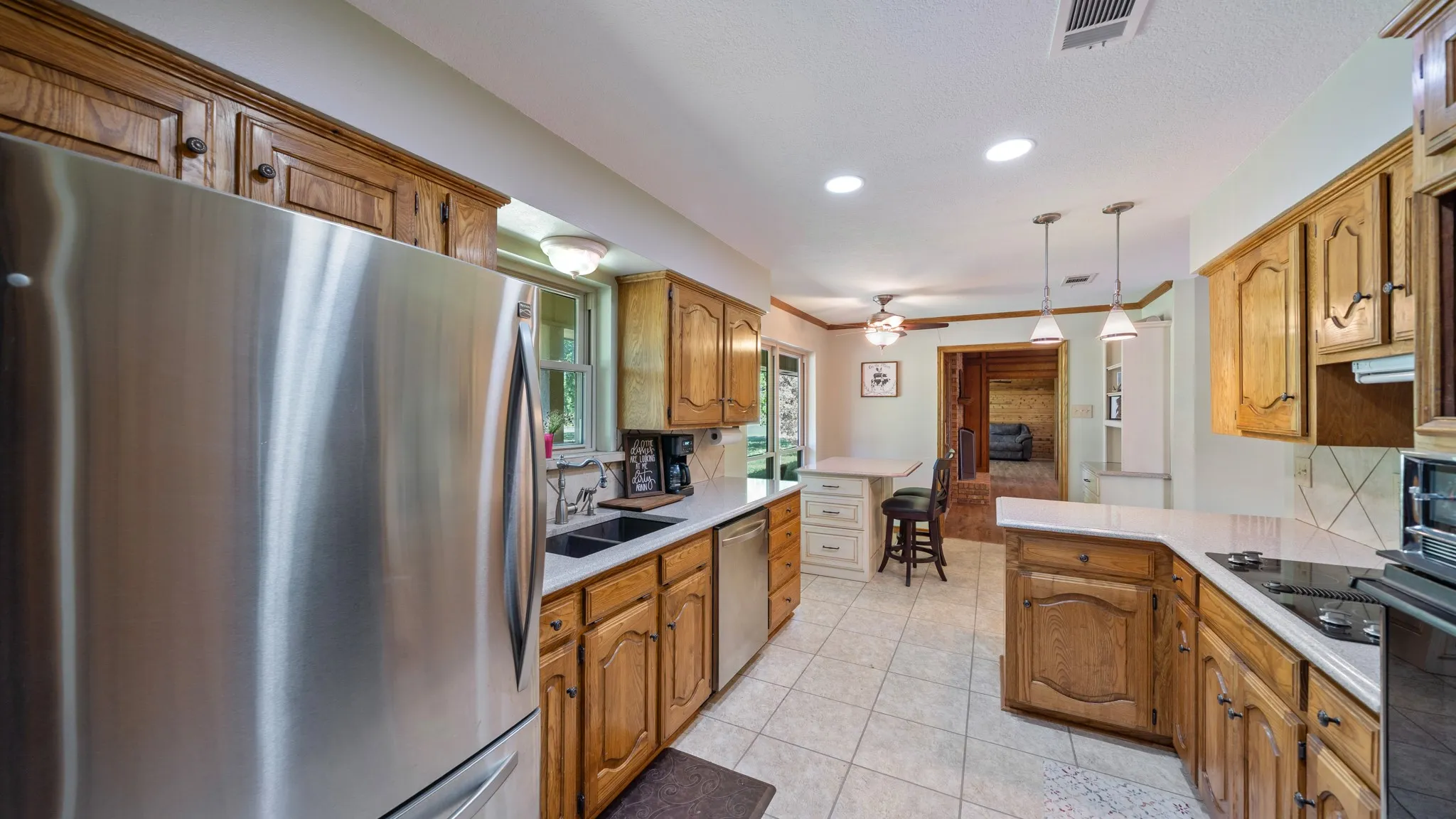 Kitchen featuring stainless steel appliances, wood finish cabinets, light tile patterned flooring, decorative light fixtures, and a peninsula