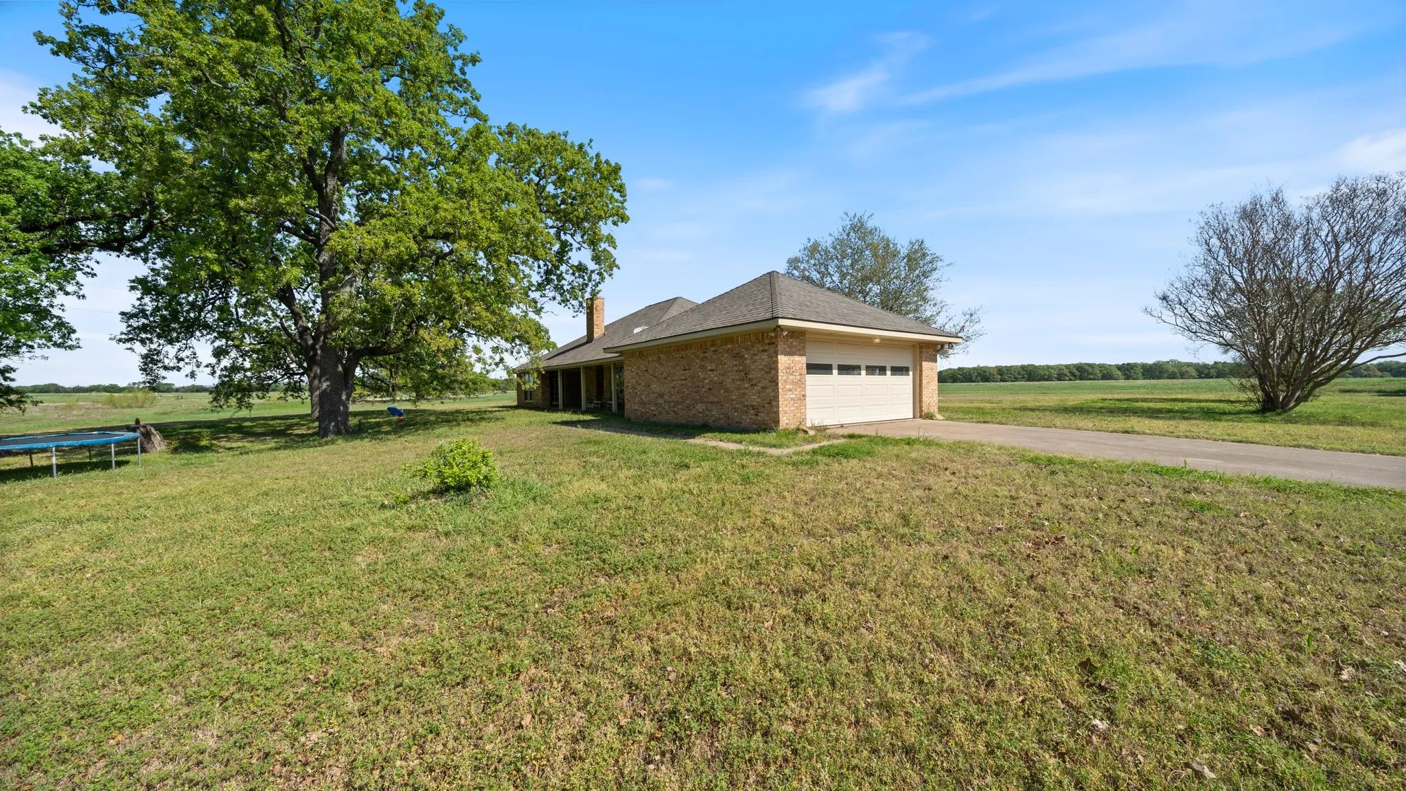 View of side of home with a lawn, brick siding, an attached garage, concrete driveway, and a rural view