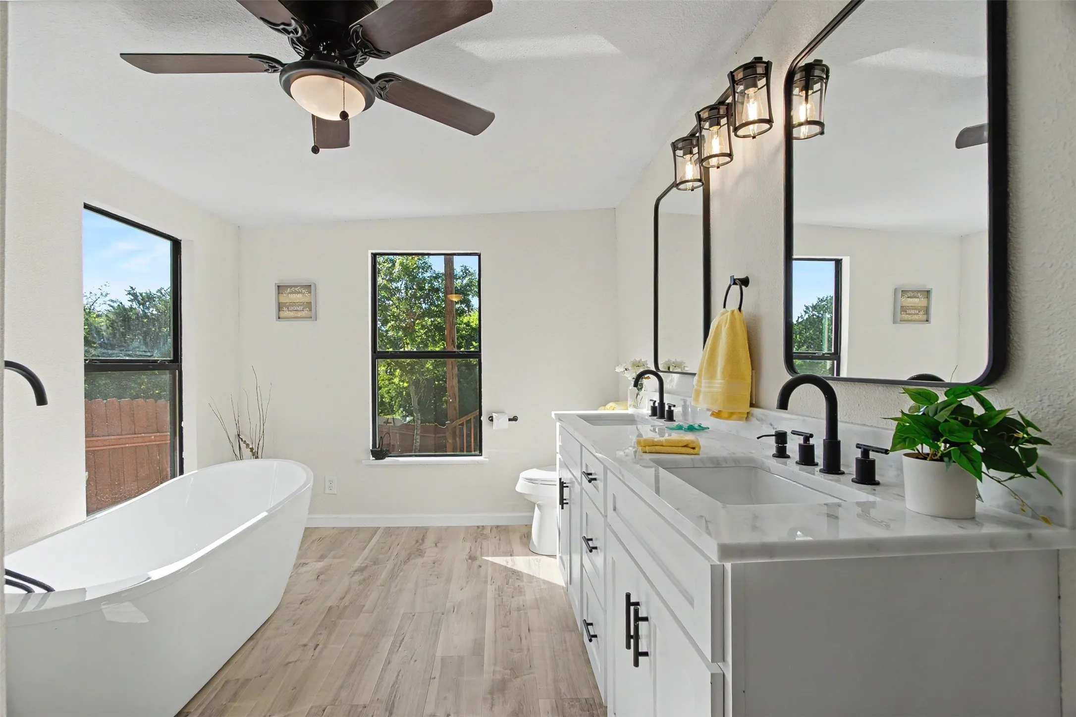 Bathroom featuring a freestanding soaking tub, dual vanity with white cabinetry, matte black fixtures, and wood-finish flooring