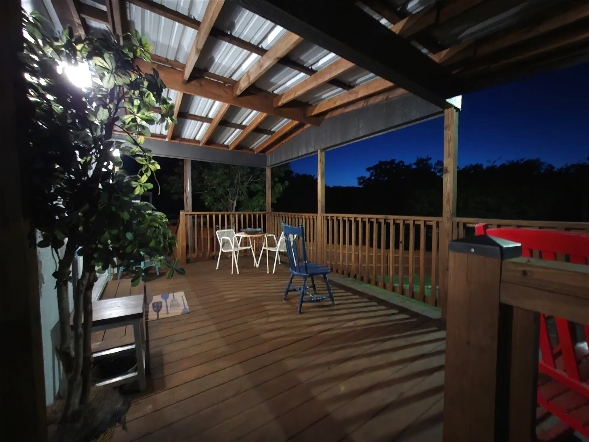 Covered outdoor deck with wood-finish flooring, wood railings, and exposed beam ceiling with a metal roof