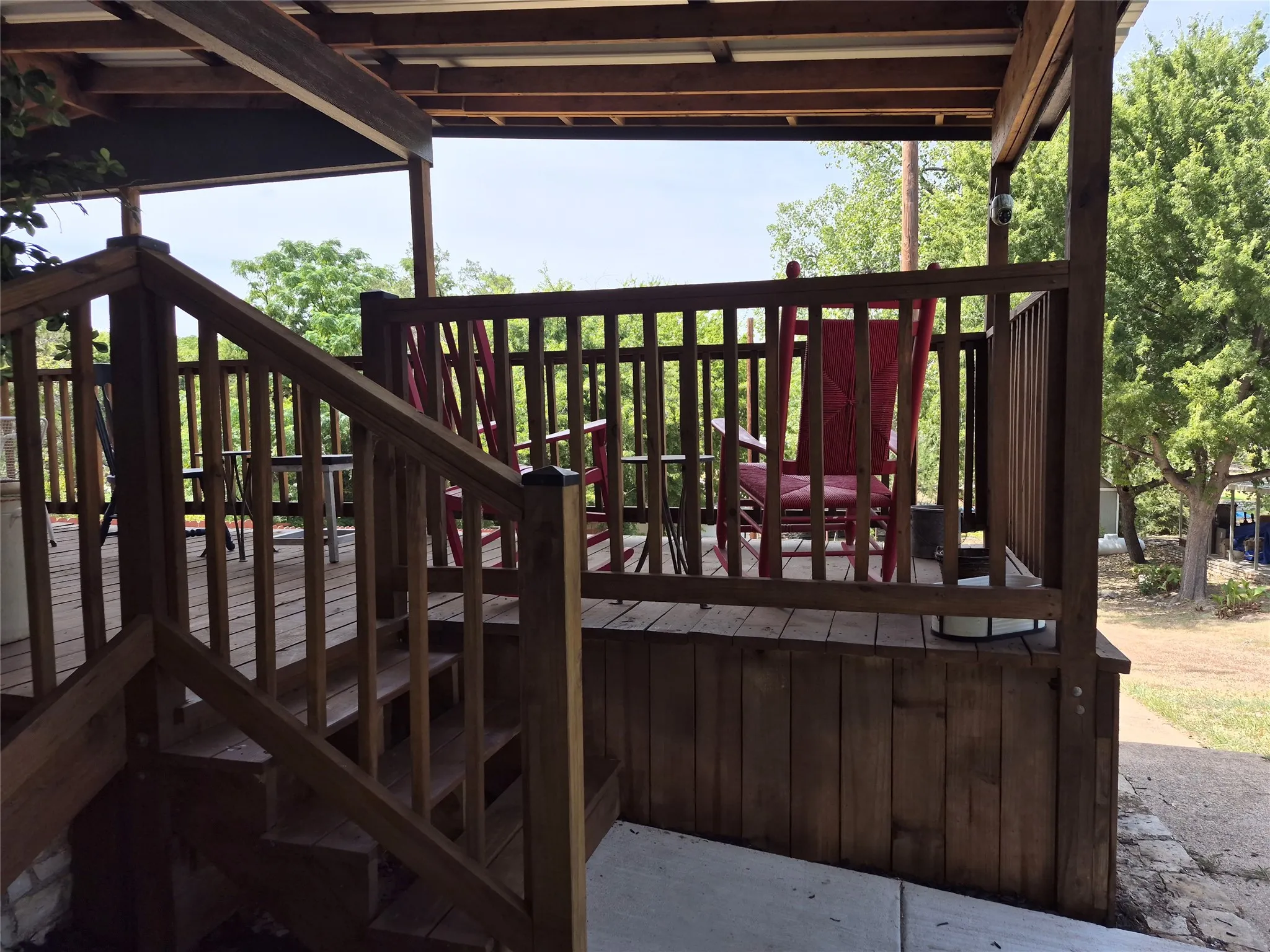 Wood-finish decking with railings and stairs, featuring a covered porch with exposed wood beams and a corrugated metal roof