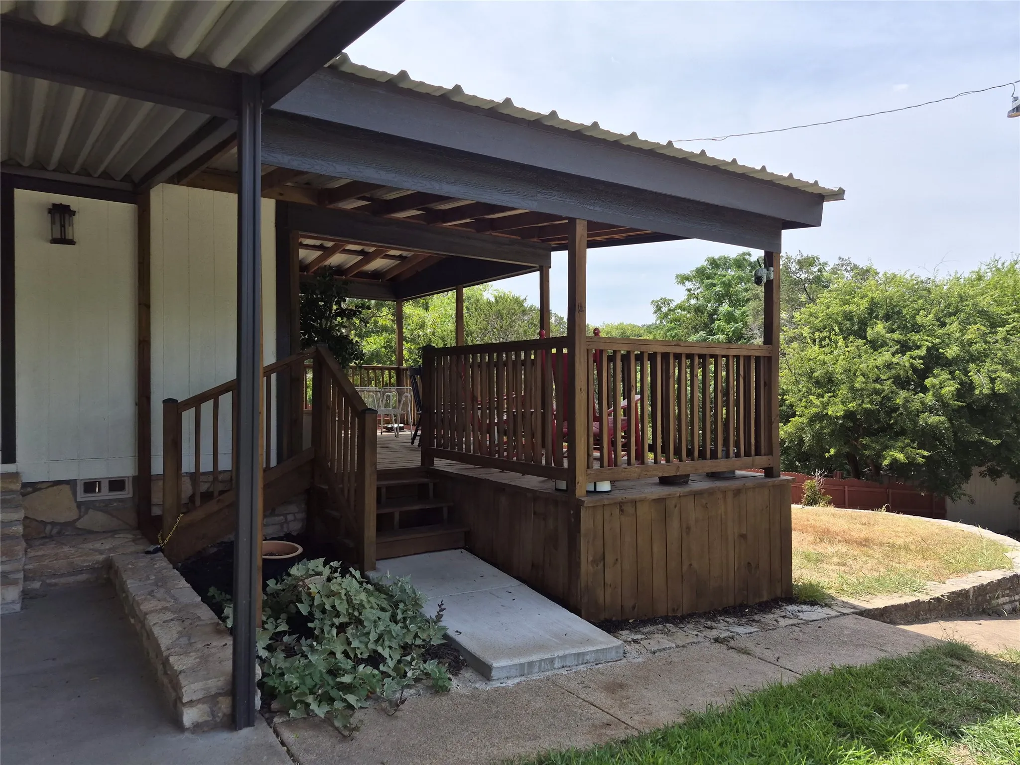 Covered front porch with wood railings, a concrete ramp, and a metal roof