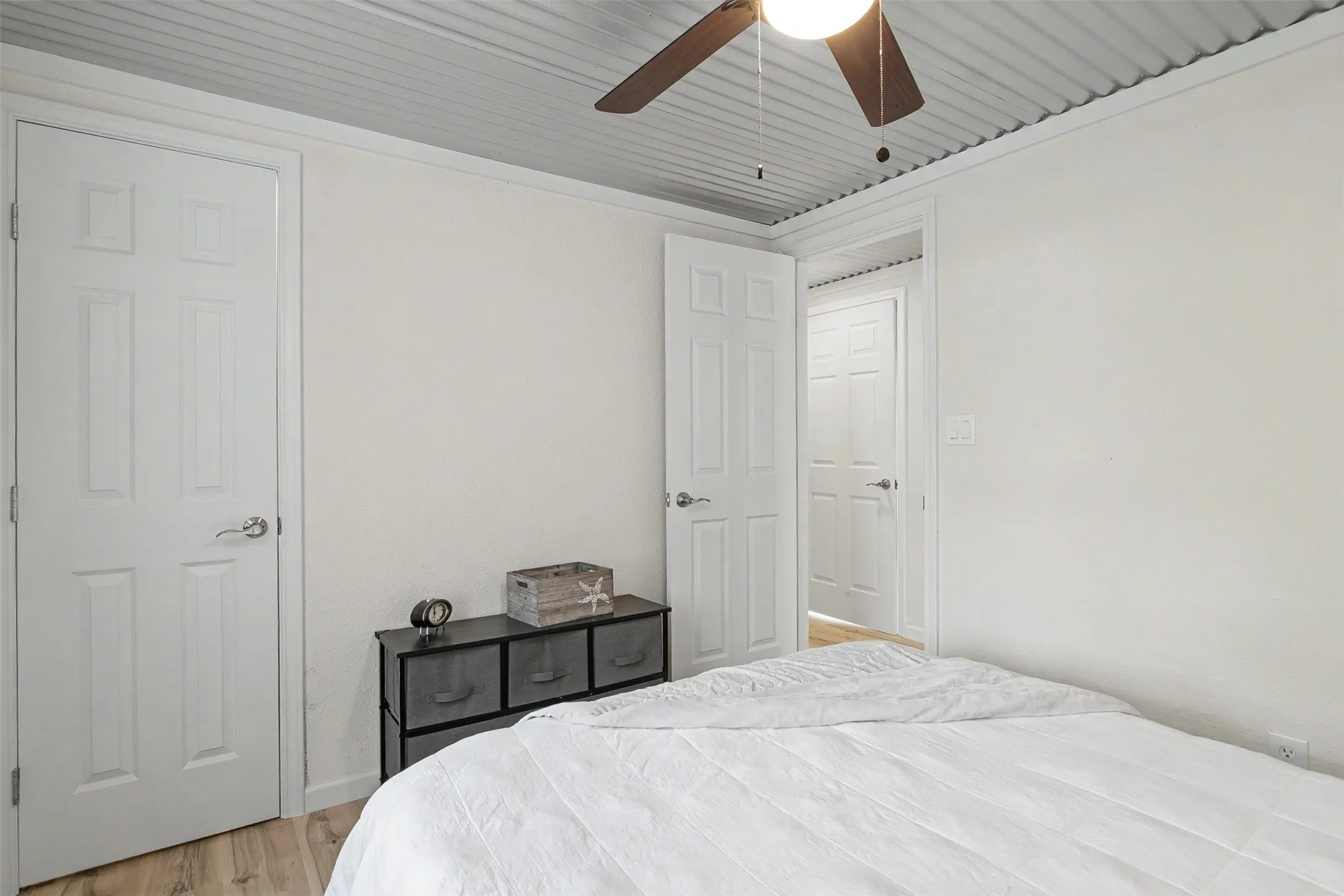 Bedroom featuring wood-finish flooring, white walls, and a corrugated metal ceiling