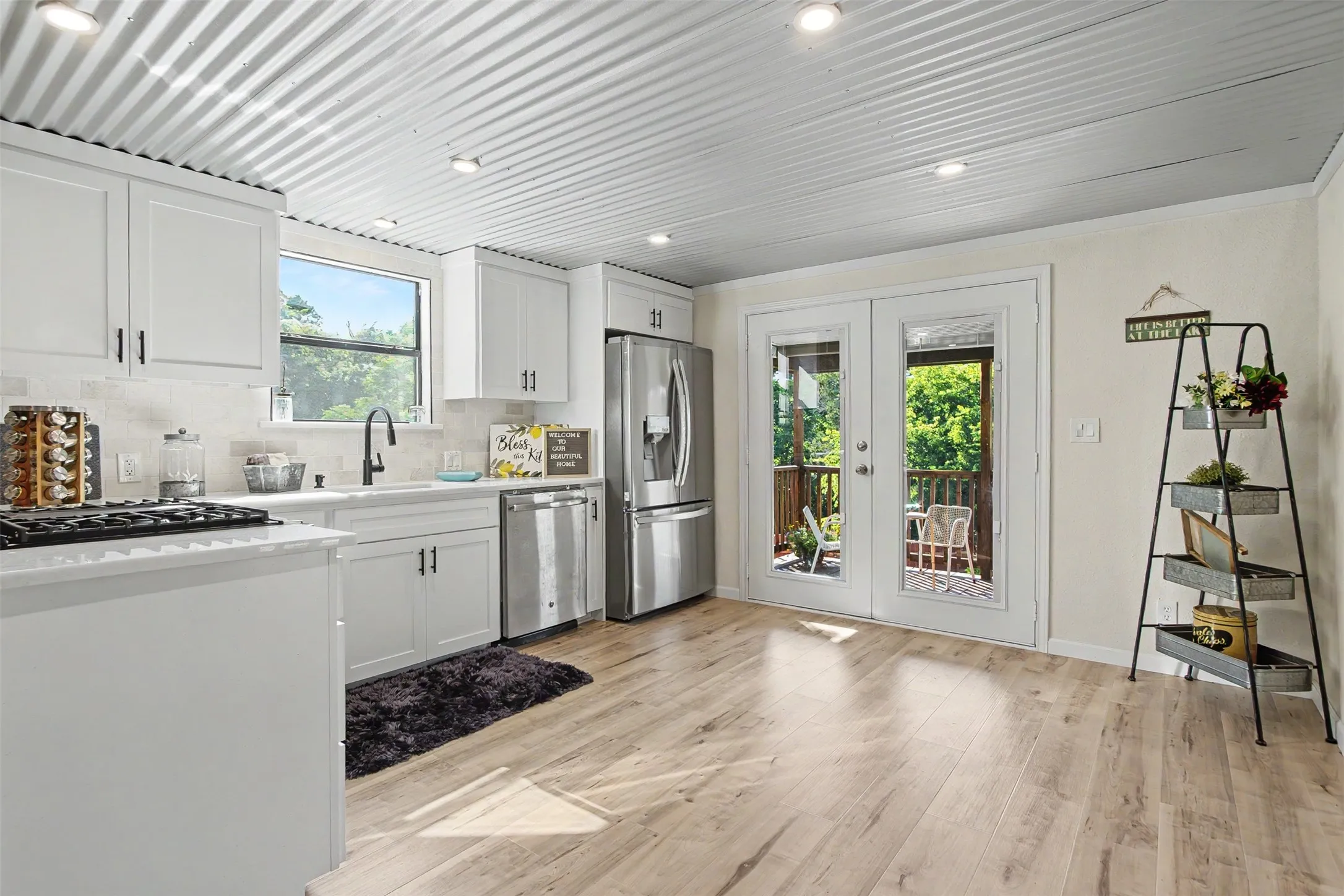 Kitchen featuring white cabinetry with black hardware, stainless steel appliances, a white tile backsplash, and light wood-finish flooring