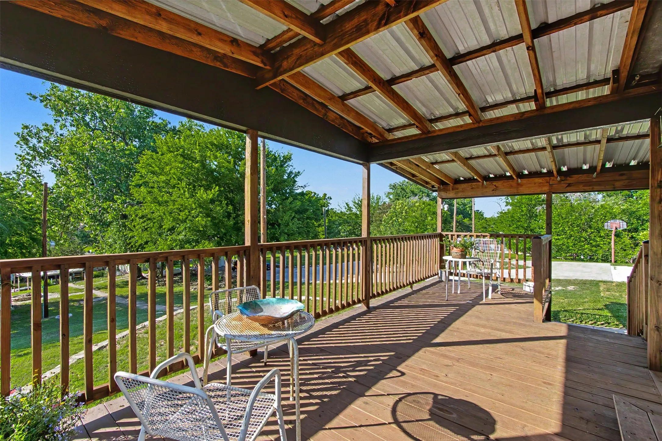 Covered outdoor deck featuring wood flooring, wood railing, exposed wood beams, and a corrugated metal ceiling