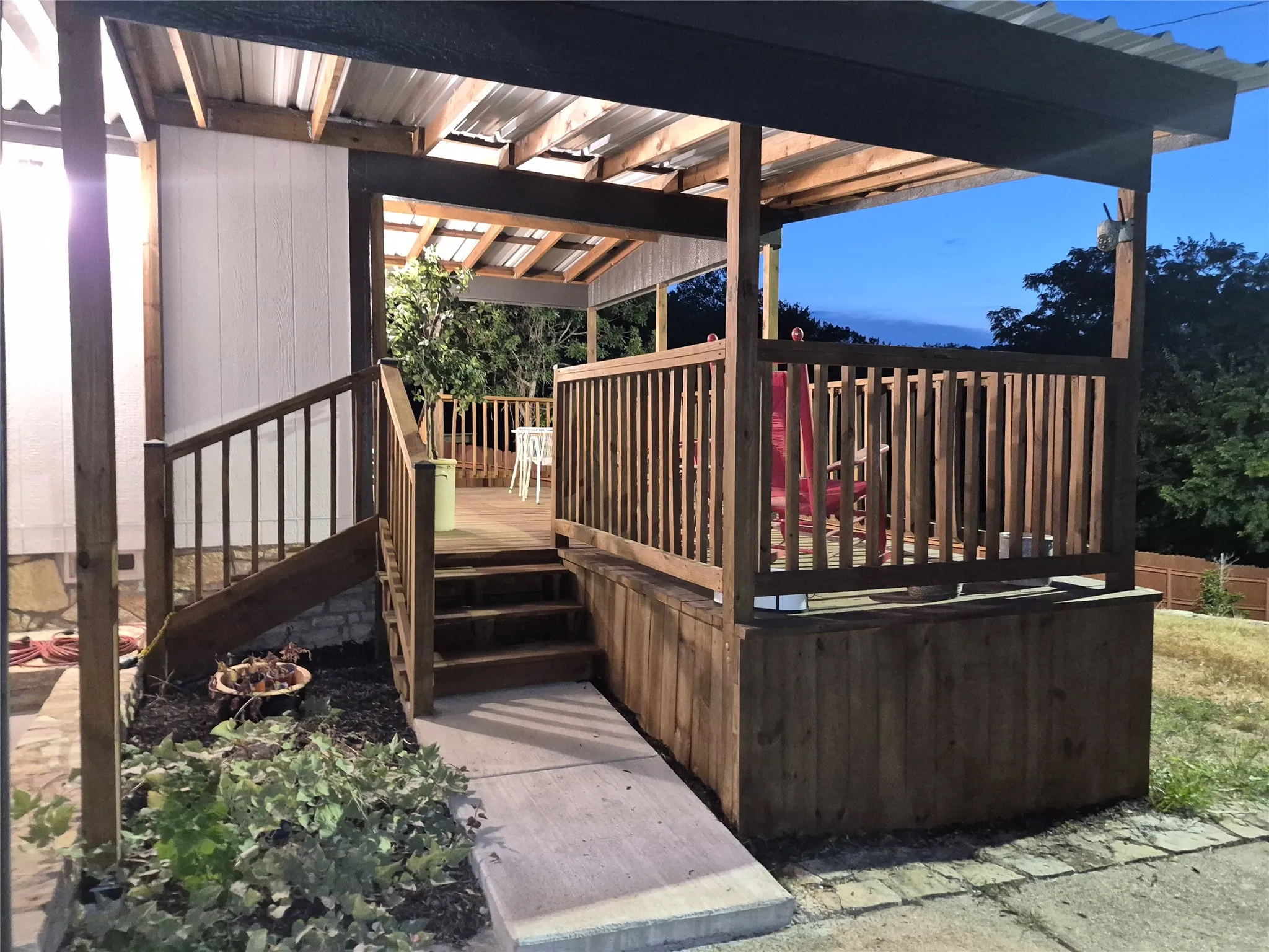 Covered outdoor deck with wood railing, wood steps, and concrete ramp access