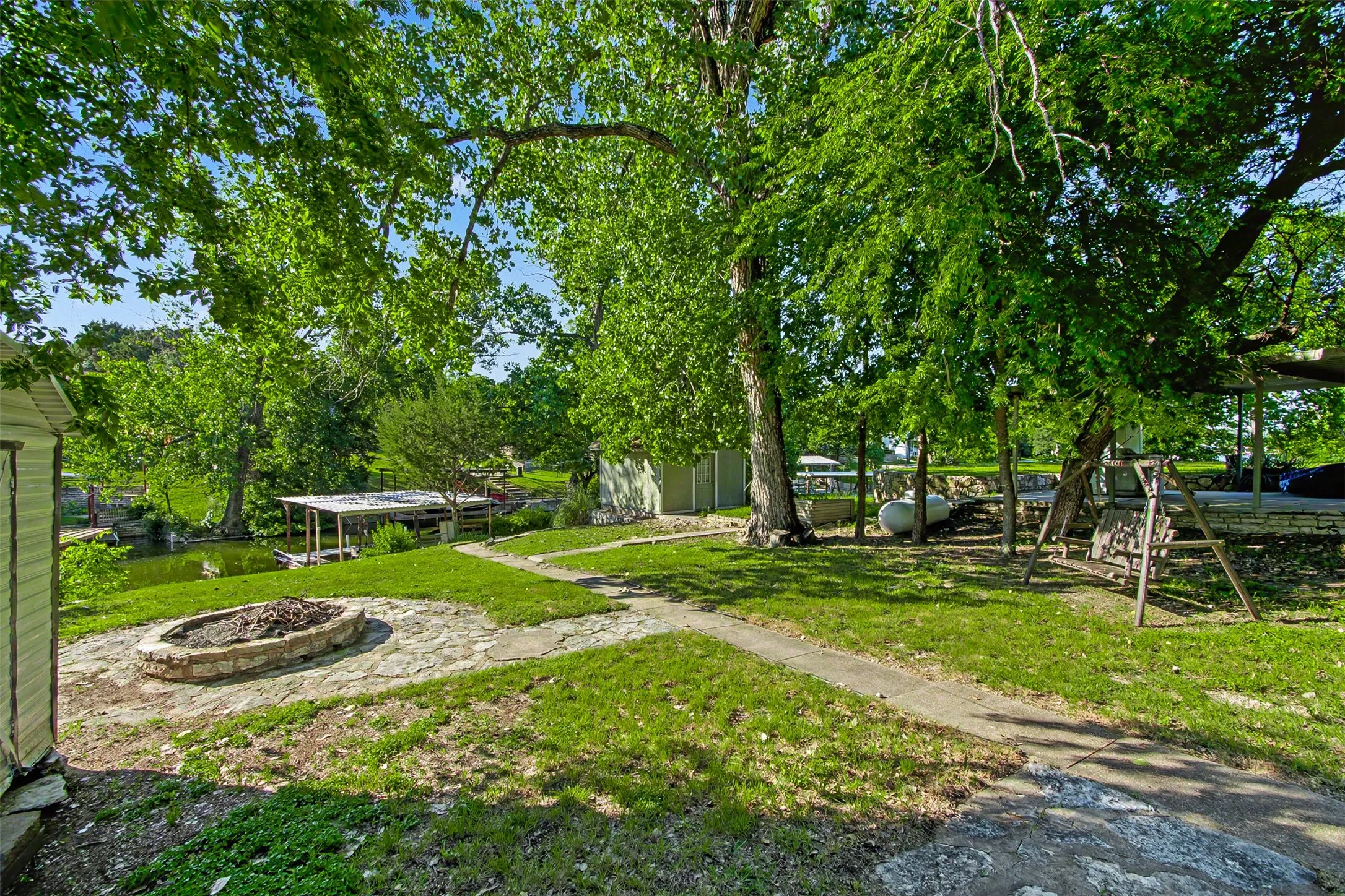 Expansive backyard with a stone fire pit, covered boat dock, and mature trees