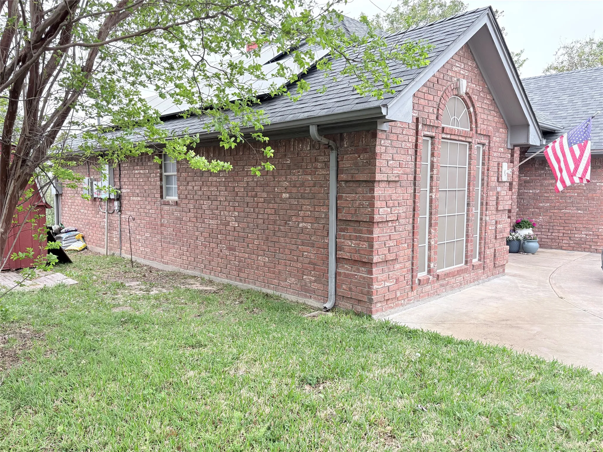 View of side of home with brick siding, a lawn, and roof with shingles