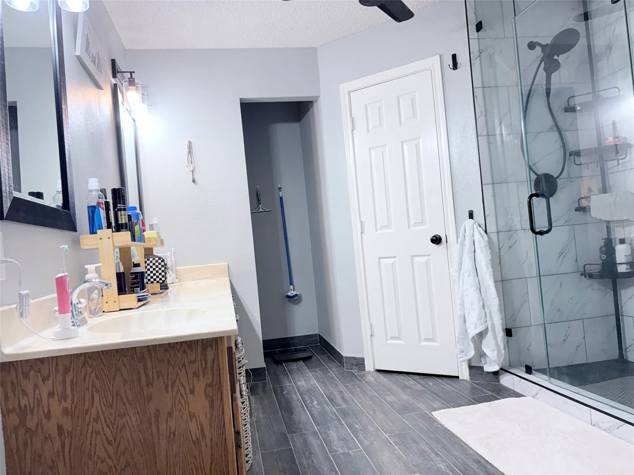 Full bath featuring vanity, a marble finish shower, a textured ceiling, and dark wood-type flooring