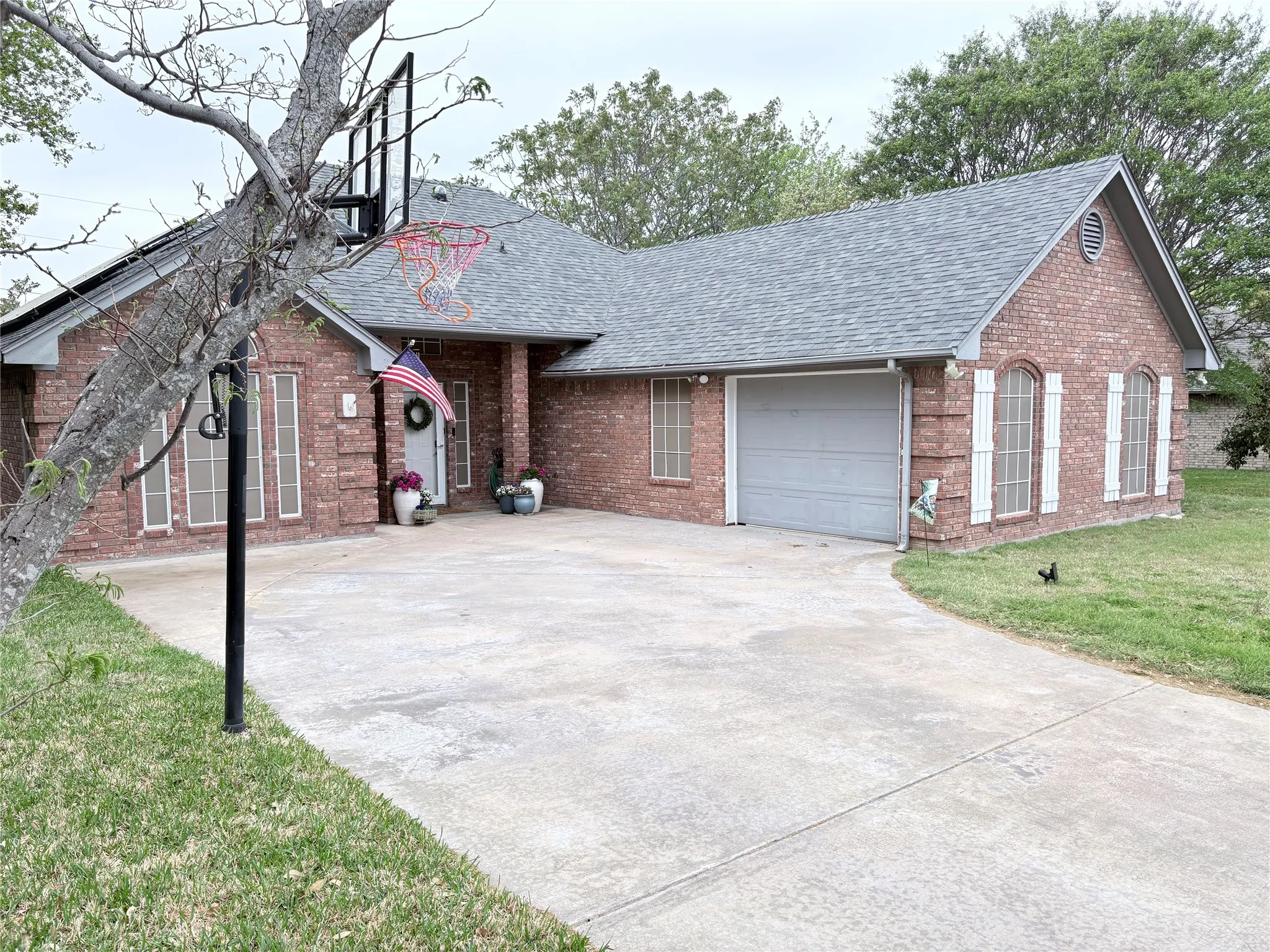 Ranch-style home with roof with shingles, brick siding, and an attached garage