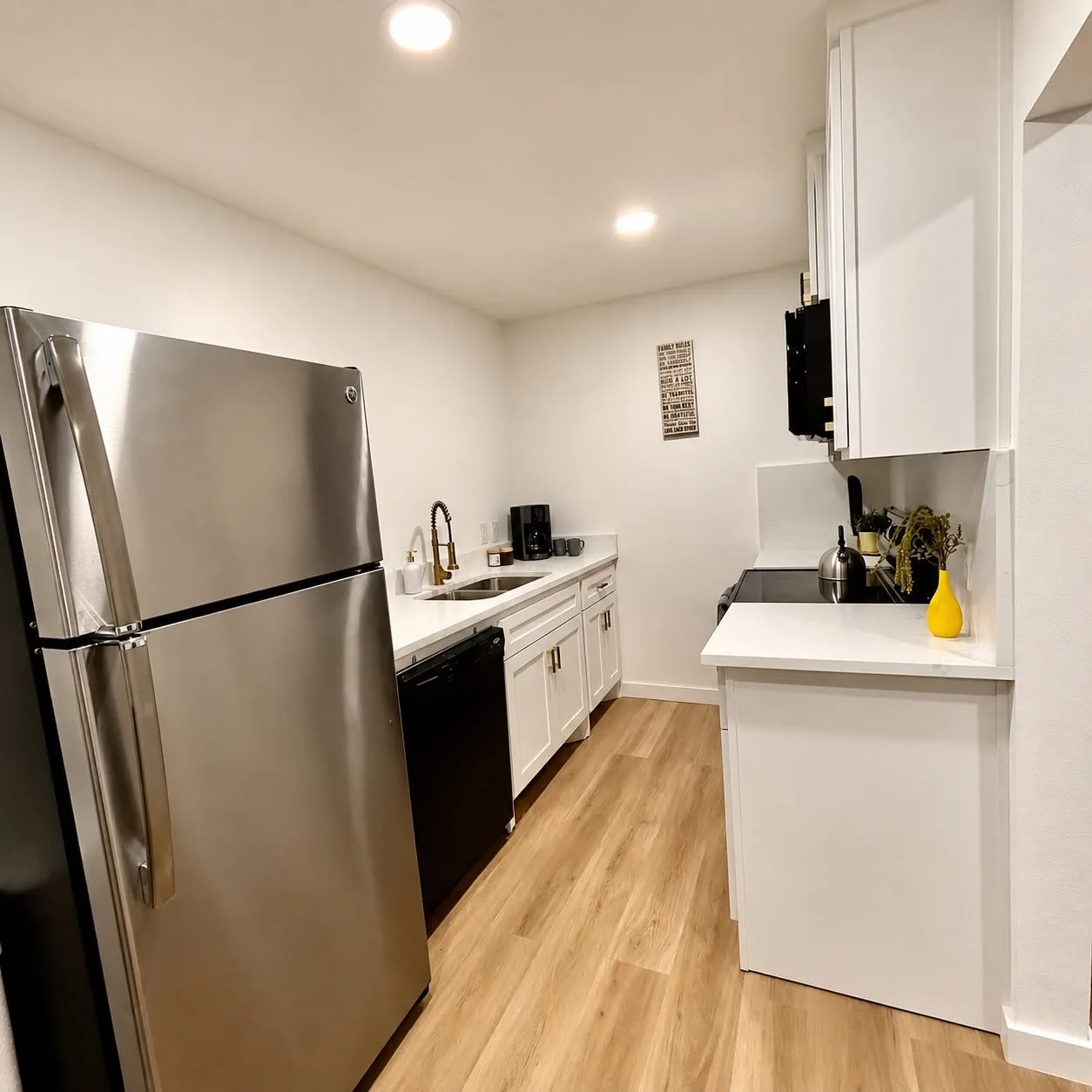 Kitchen featuring stainless steel refrigerator, white cabinetry, integrated sink with dark-finish faucet, white countertops, and wood-finish flooring