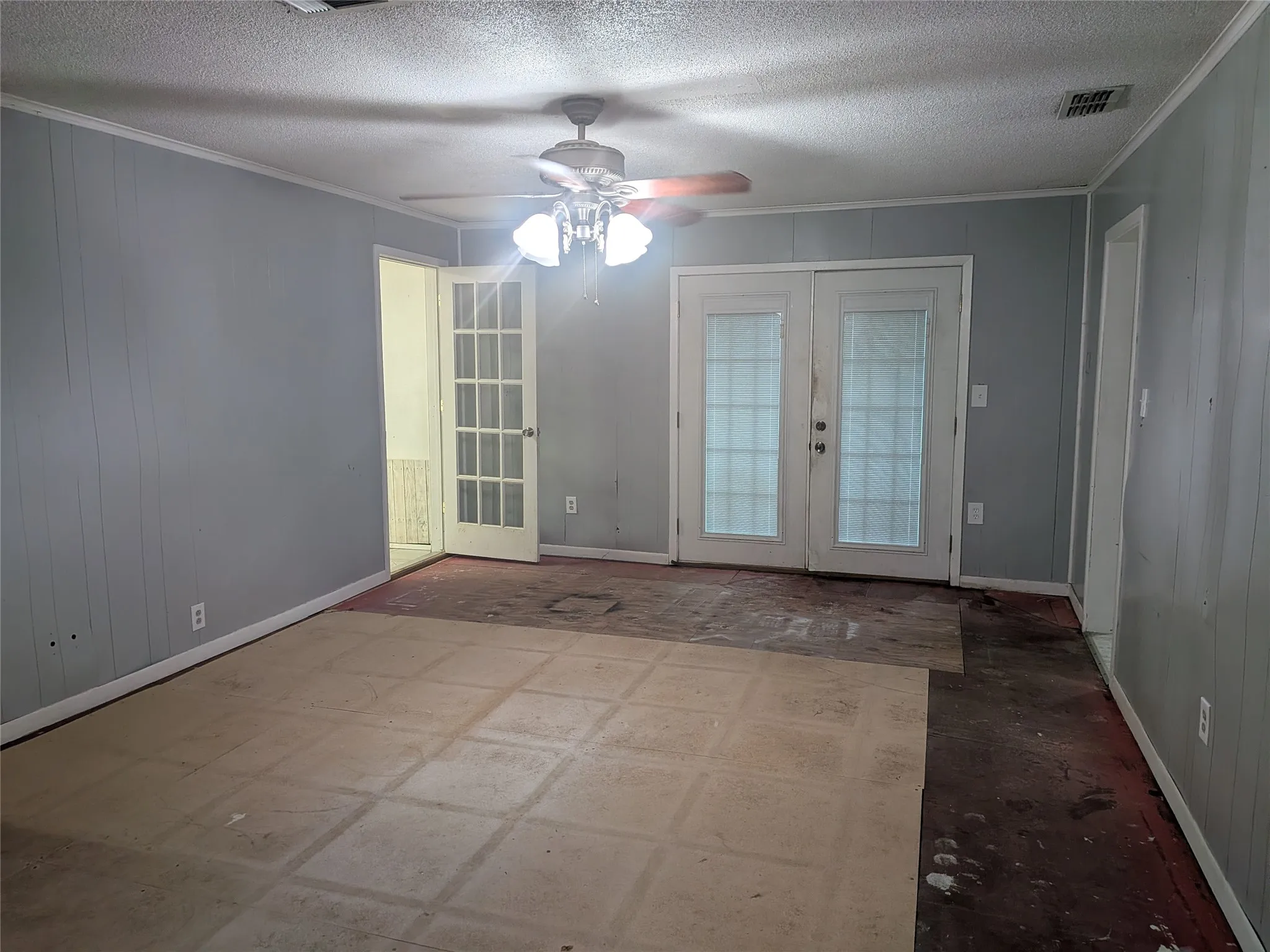 Empty room with french doors, crown molding, a ceiling fan, a textured ceiling, and wooden walls