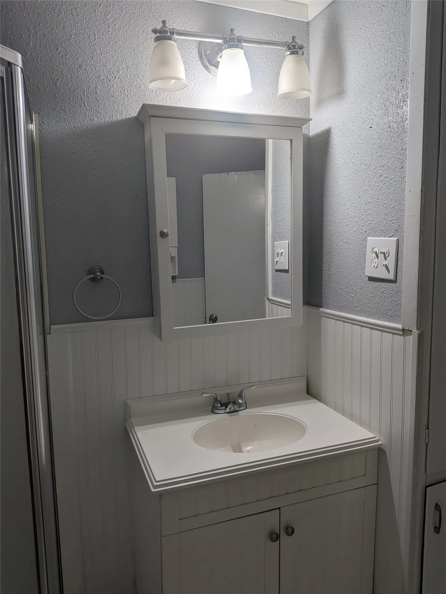 Bathroom with a textured wall, vanity, and wainscoting