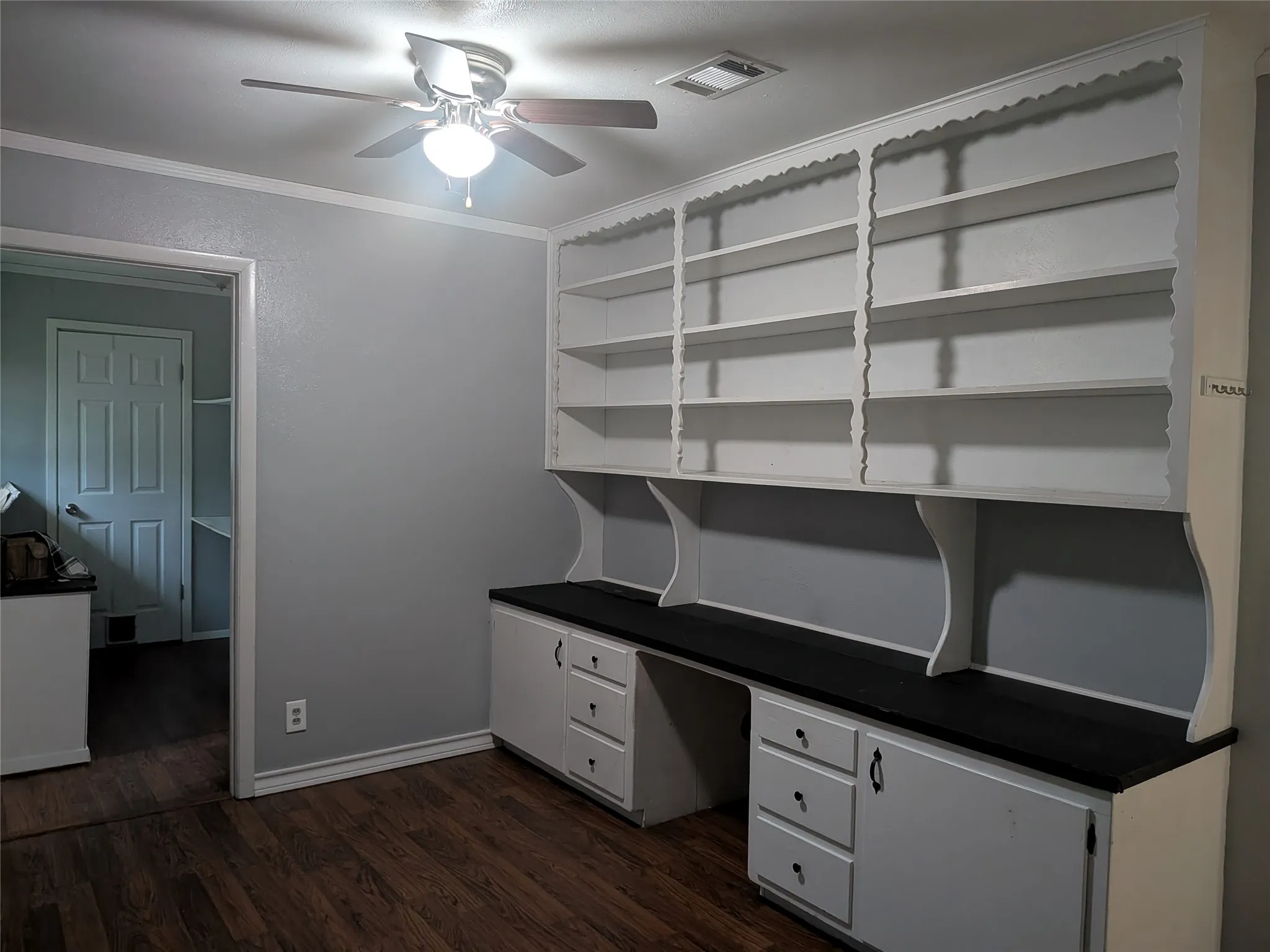 Unfurnished office featuring a ceiling fan, dark wood-style flooring, crown molding, and built in desk