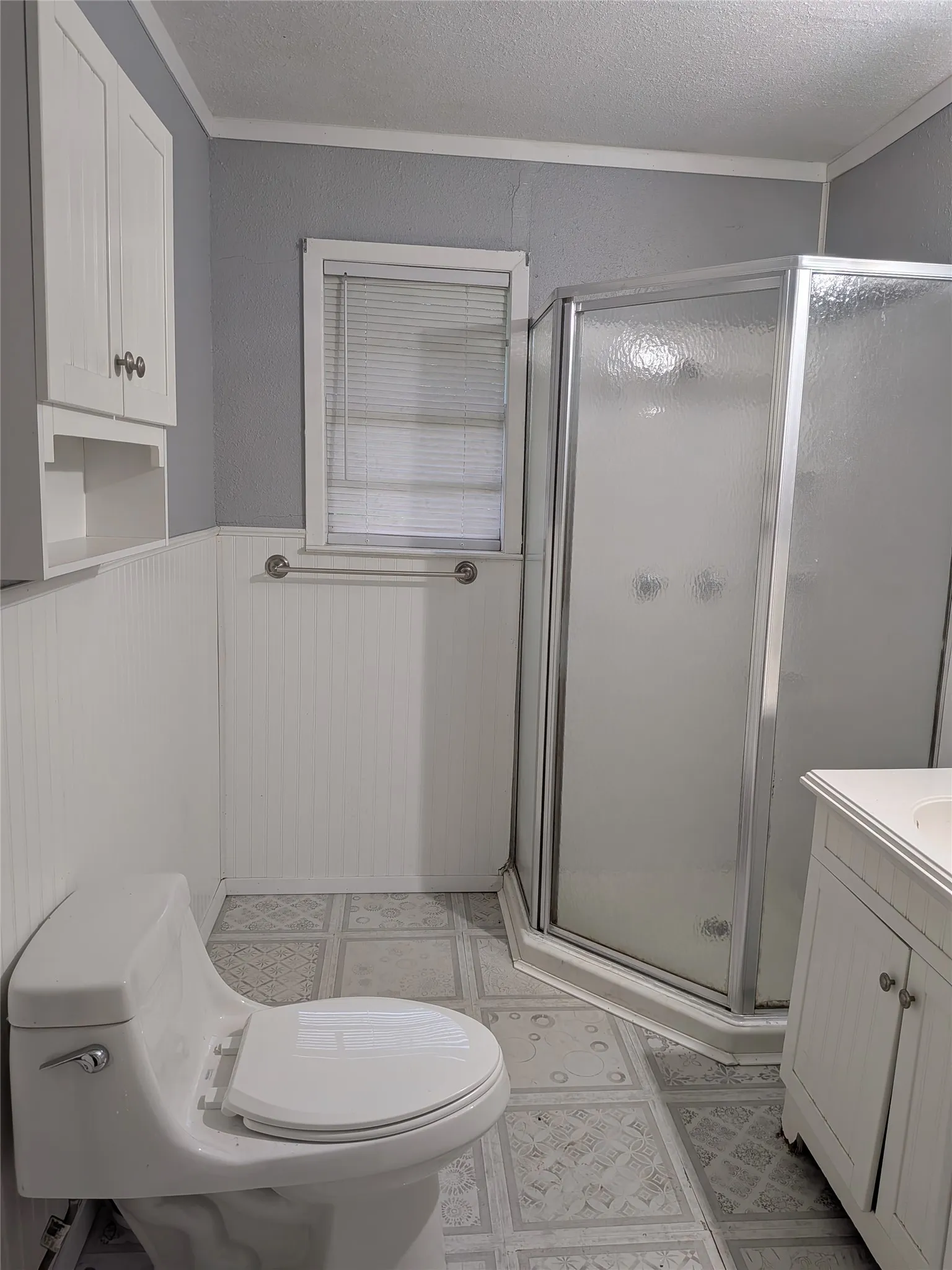 Bathroom with vanity, a stall shower, ornamental molding, a wainscoted wall, and a textured ceiling