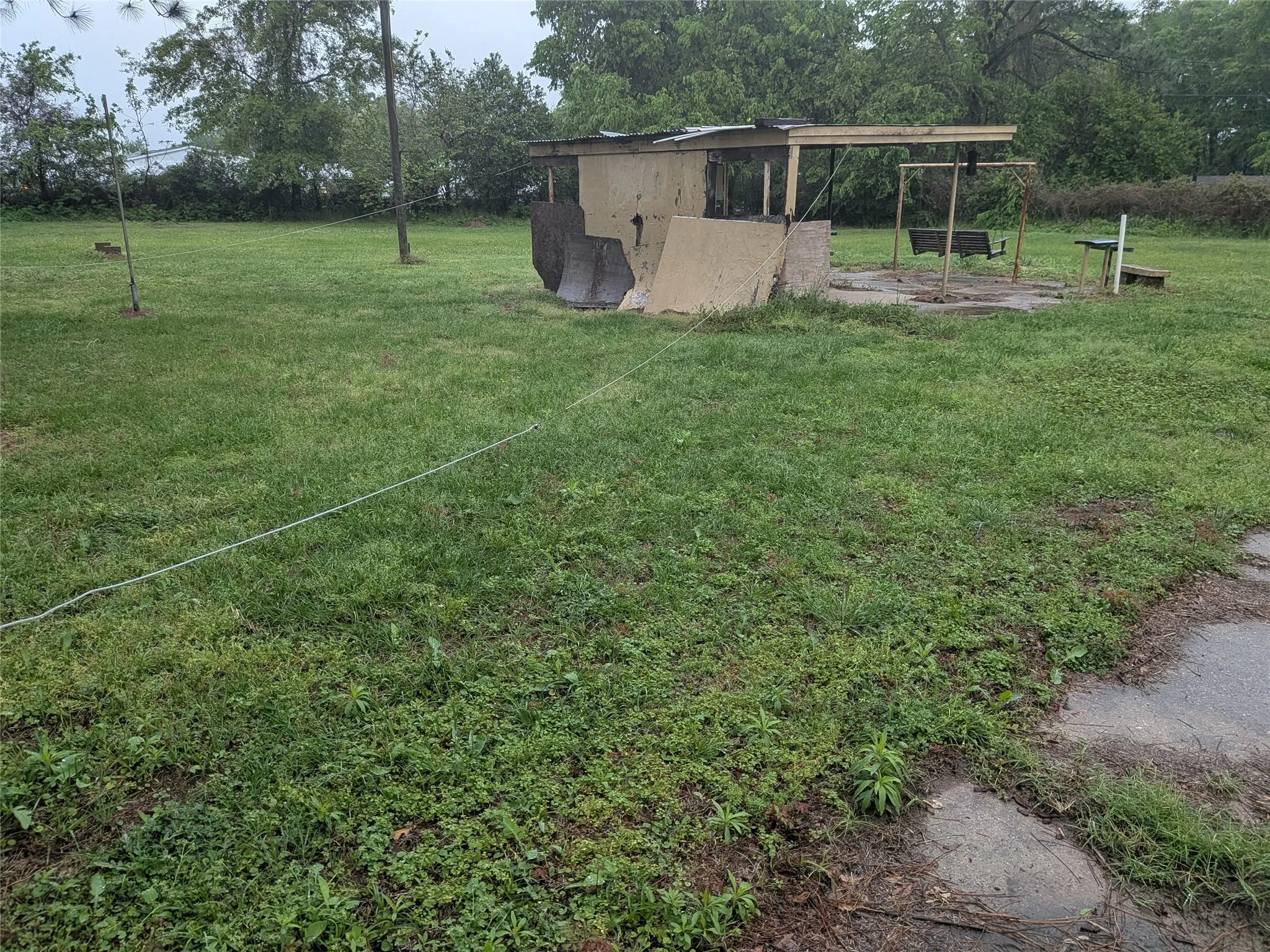 View of grassy yard featuring an outbuilding, view of wooded area, and a patio