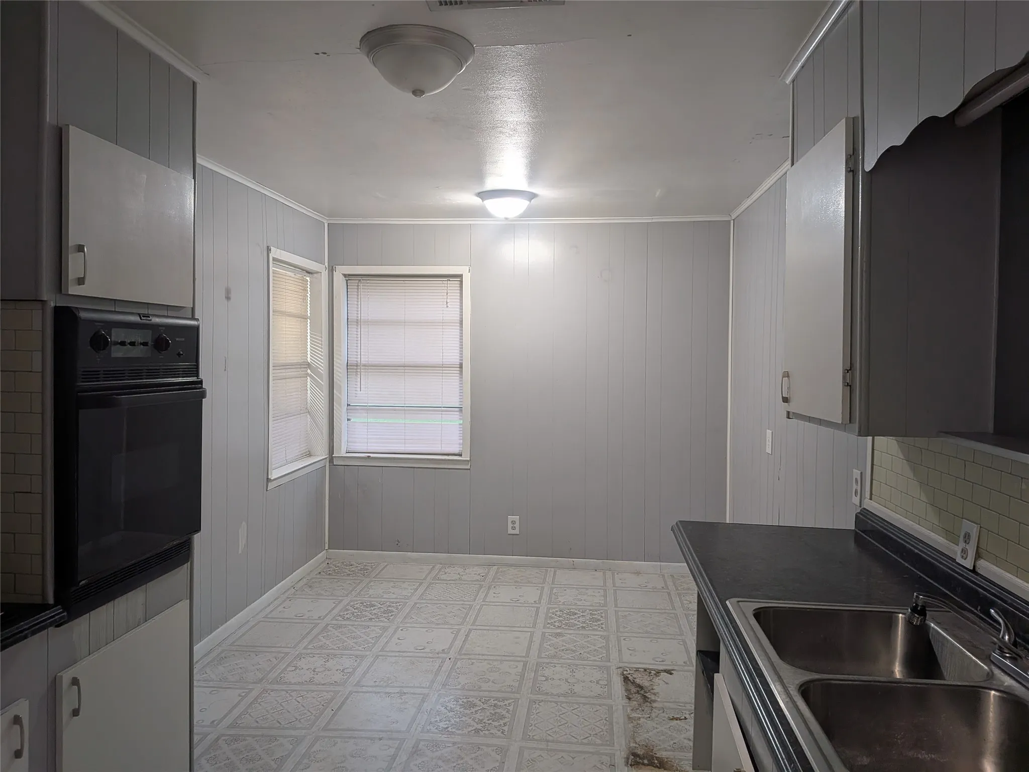 Kitchen featuring light flooring, dark countertops, black oven, wooden walls, and gray cabinetry