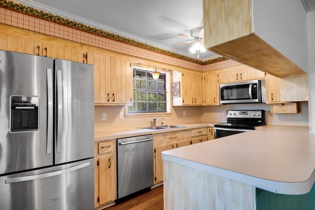 Kitchen with stainless steel appliances, a peninsula, light wood finish cabinets, light countertops, and crown molding