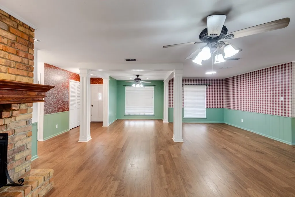 Unfurnished living room featuring wallpapered walls, wainscoting, wood finished floors, decorative columns, and a fireplace