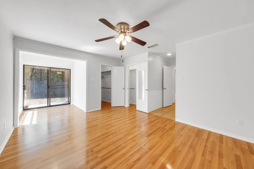 Unfurnished bedroom with a spacious closet, crown molding, access to exterior, a ceiling fan, and light wood-type flooring