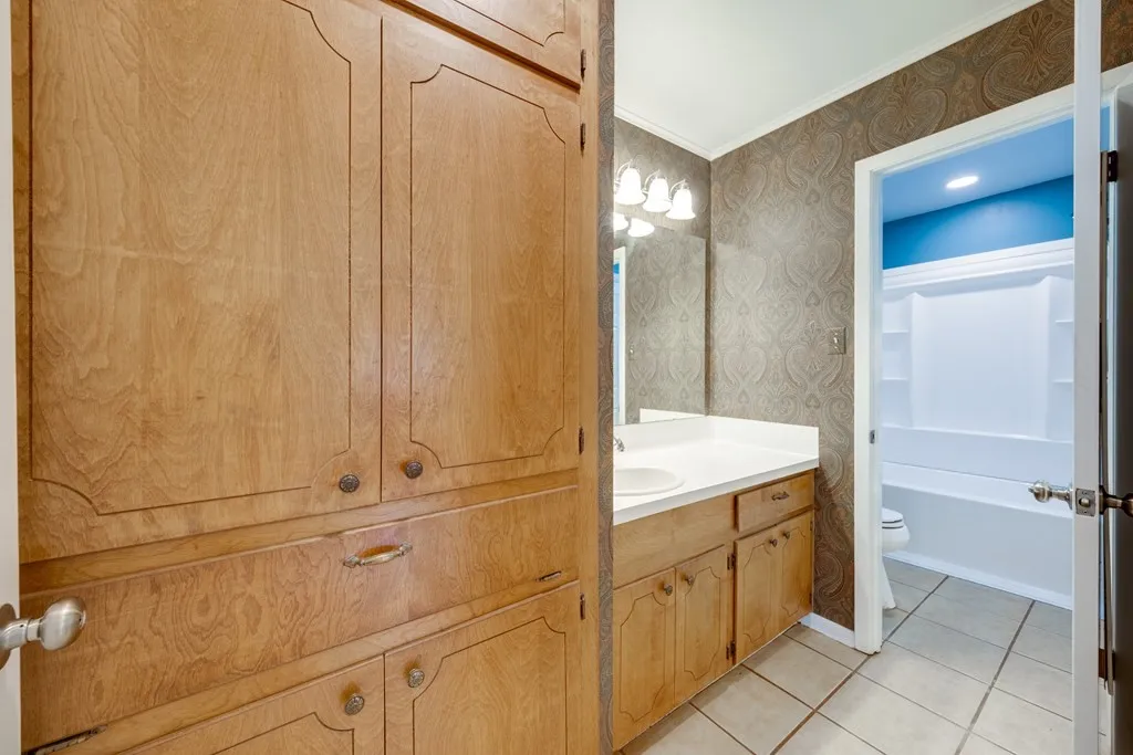 Full bath featuring wallpapered walls, vanity, light tile patterned floors, and ornamental molding