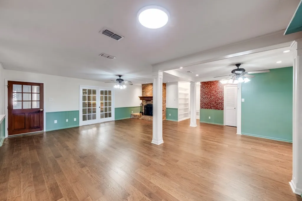 Unfurnished living room featuring a ceiling fan, dark wood-style floors, french doors, a brick fireplace, and wainscoting