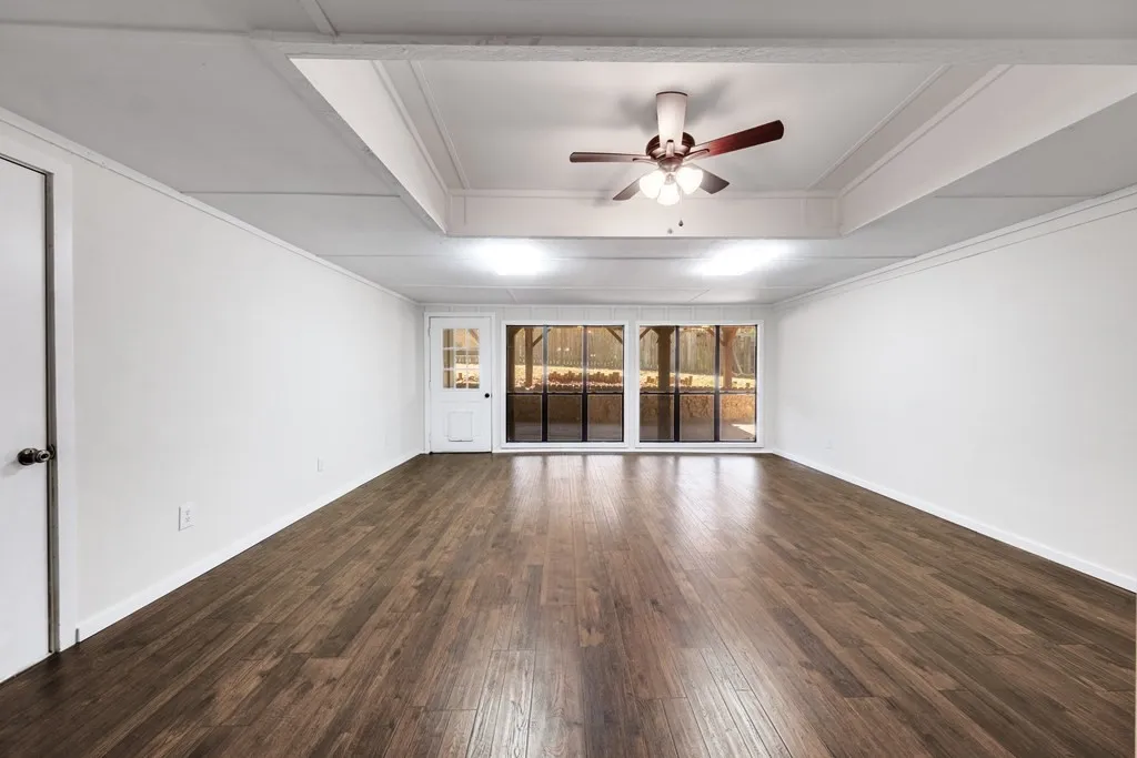 Empty room with a ceiling fan, dark wood-style floors, and a raised ceiling