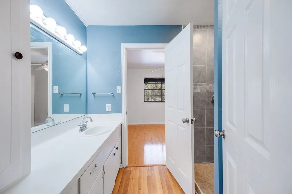 Full bath featuring light wood-style floors, vanity, and tiled shower