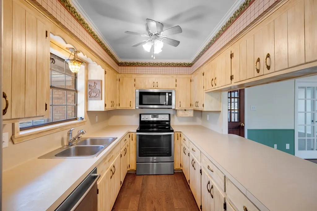 Kitchen featuring stainless steel appliances, light countertops, dark wood-style floors, ornamental molding, and ceiling fan