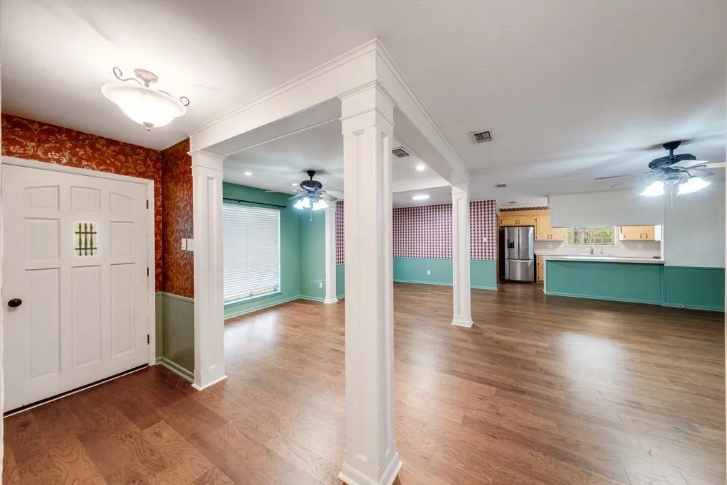 Foyer with ceiling fan, decorative columns, wallpapered walls, dark wood finished floors, and a wainscoted wall