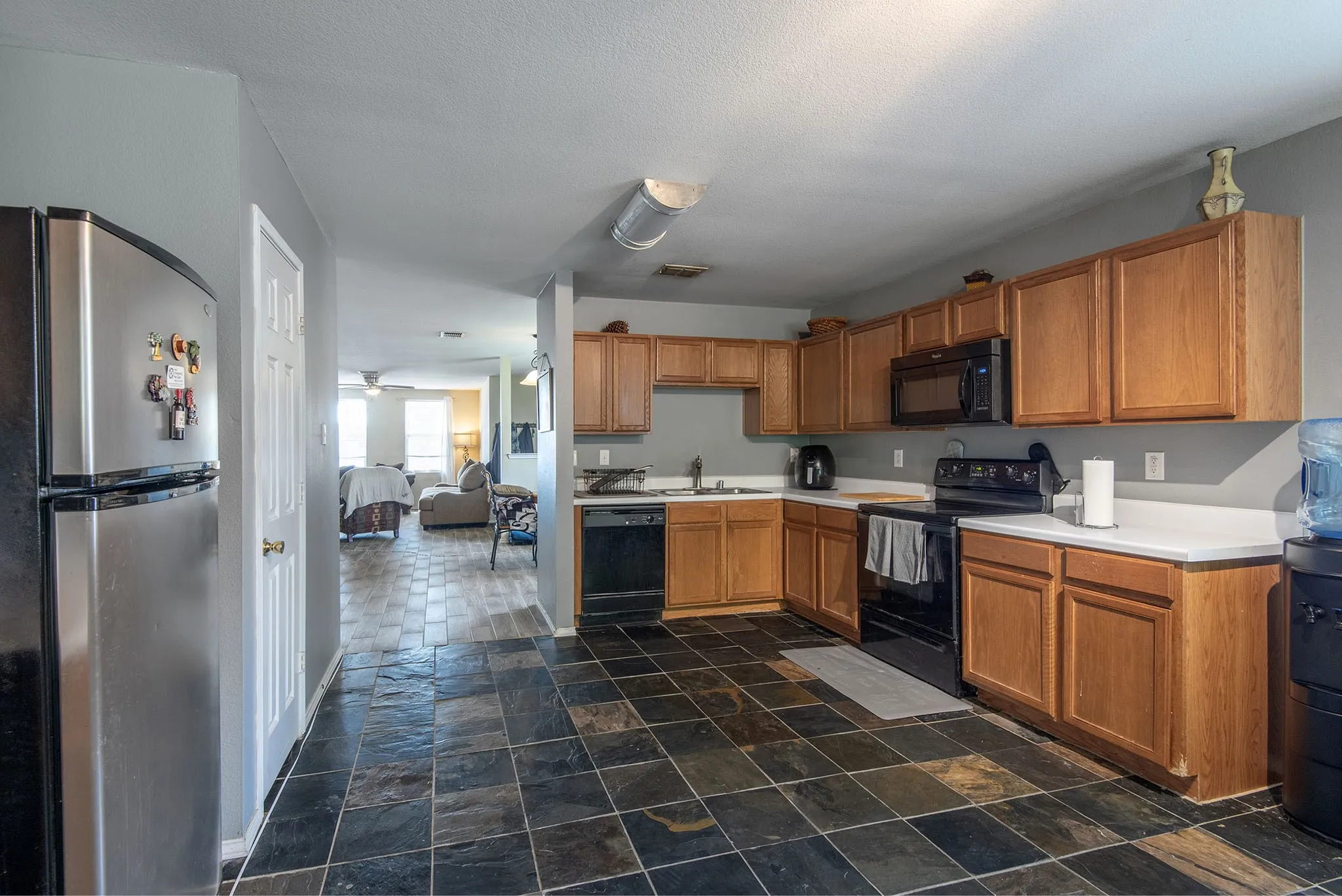 Kitchen with black appliances, light countertops, wood finish cabinetry, and dark stone finish flooring