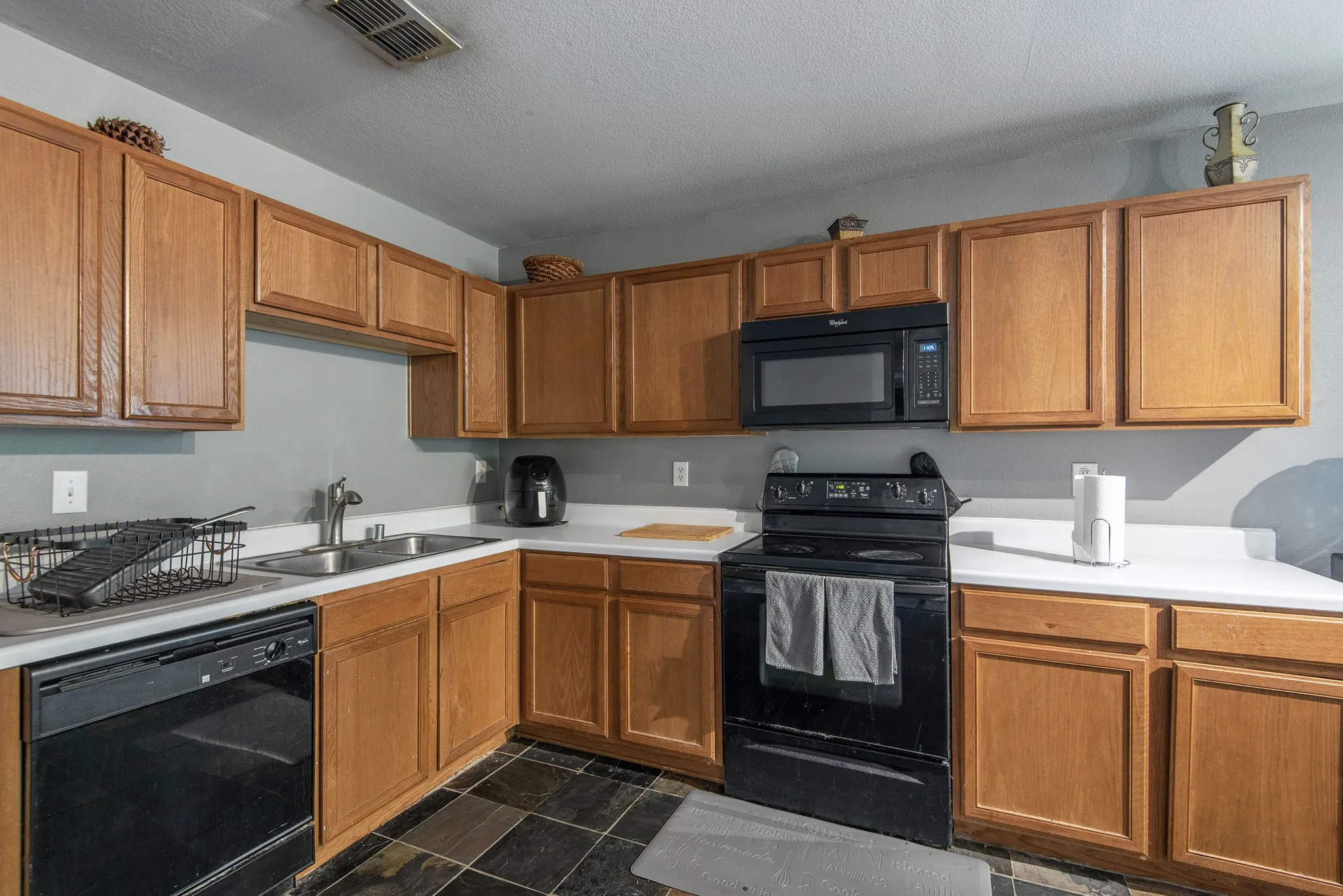 Kitchen with black appliances, light countertops, wood finish cabinetry, dark stone finish flooring, and a textured ceiling