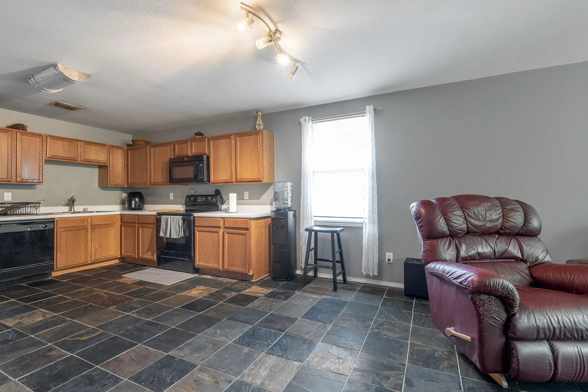 Kitchen featuring black appliances, wood finish cabinetry, light countertops, stone tile floors, and open floor plan