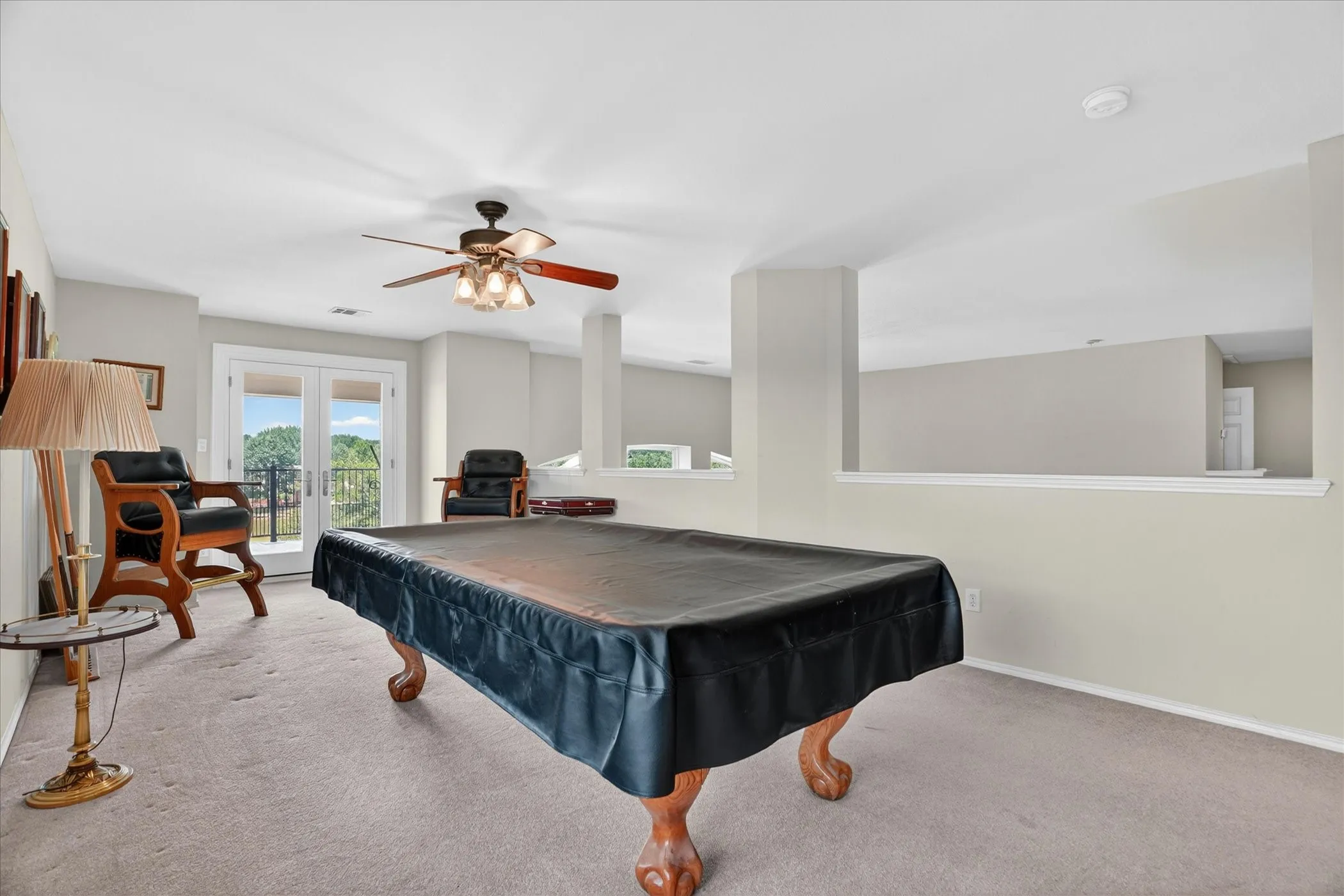 Spacious entertainment area featuring carpet flooring, an open wall cut-out, ceiling fan with integrated lighting, and a double-door exterior entrance
