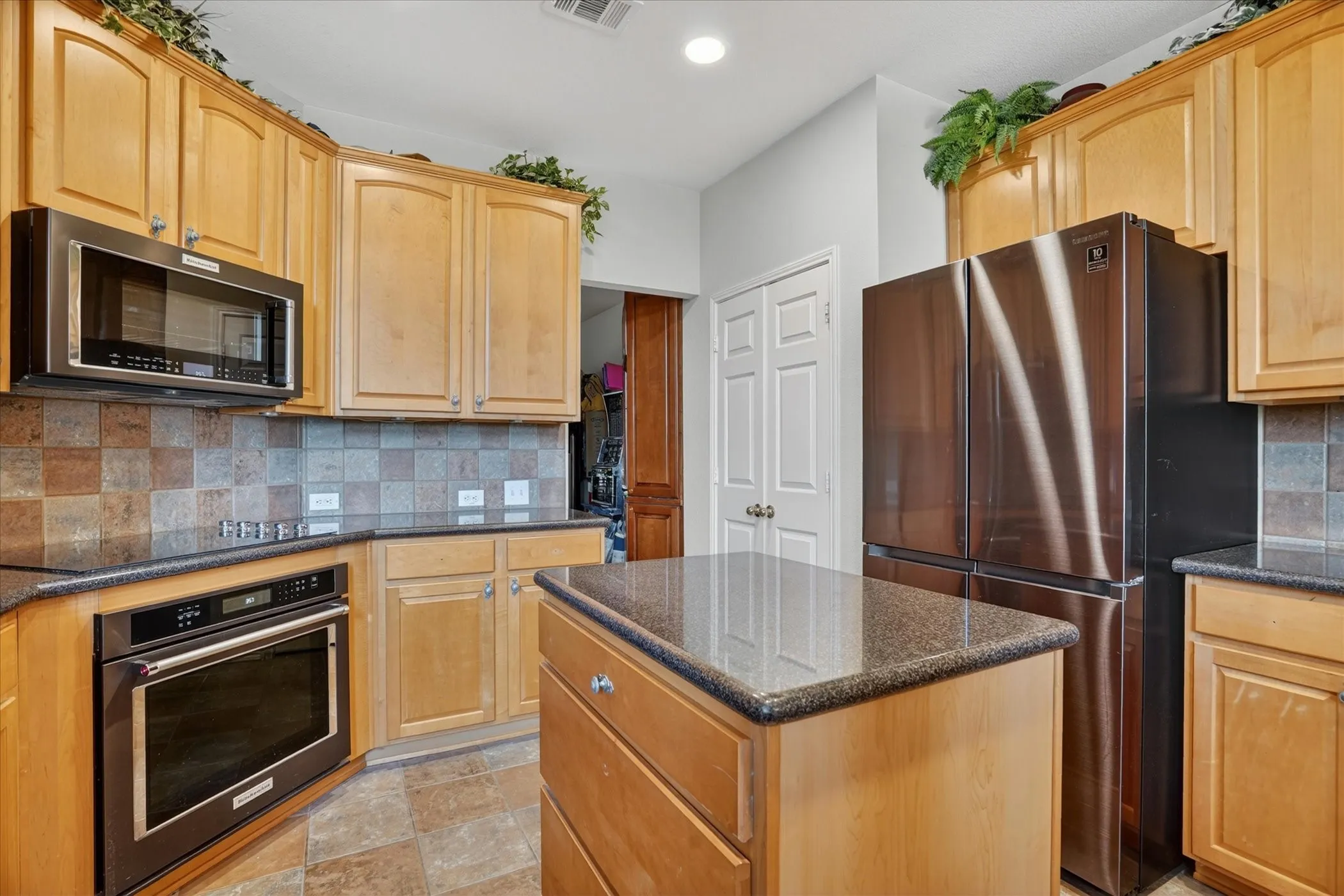 Kitchen featuring light wood cabinetry, dark countertops, built-in microwave, and stainless steel refrigerator