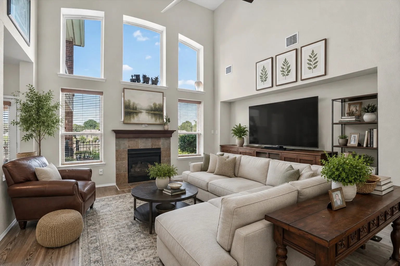 Virtually Staged Two-story living area featuring a tile-surround fireplace with wood mantel, a wall of high windows, and wood-finish flooring