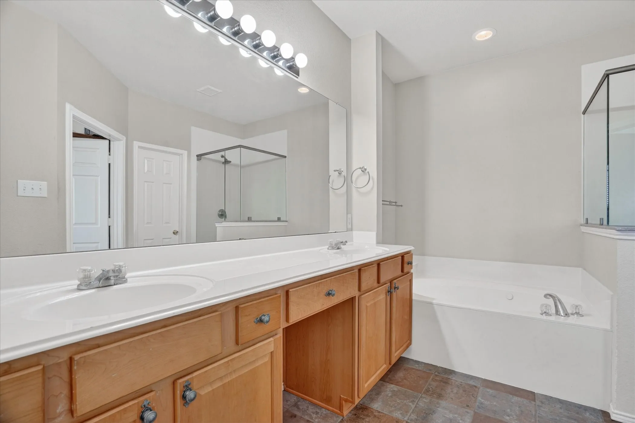 Dual vanity with white undermount sinks and light wood cabinetry, featuring a large wall-mounted mirror and overhead strip lighting