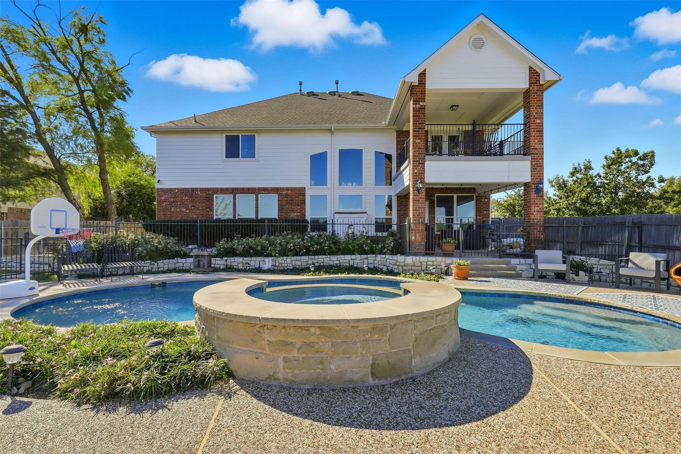 Back of house with a balcony, a patio, brick siding, and a pool with connected hot tub