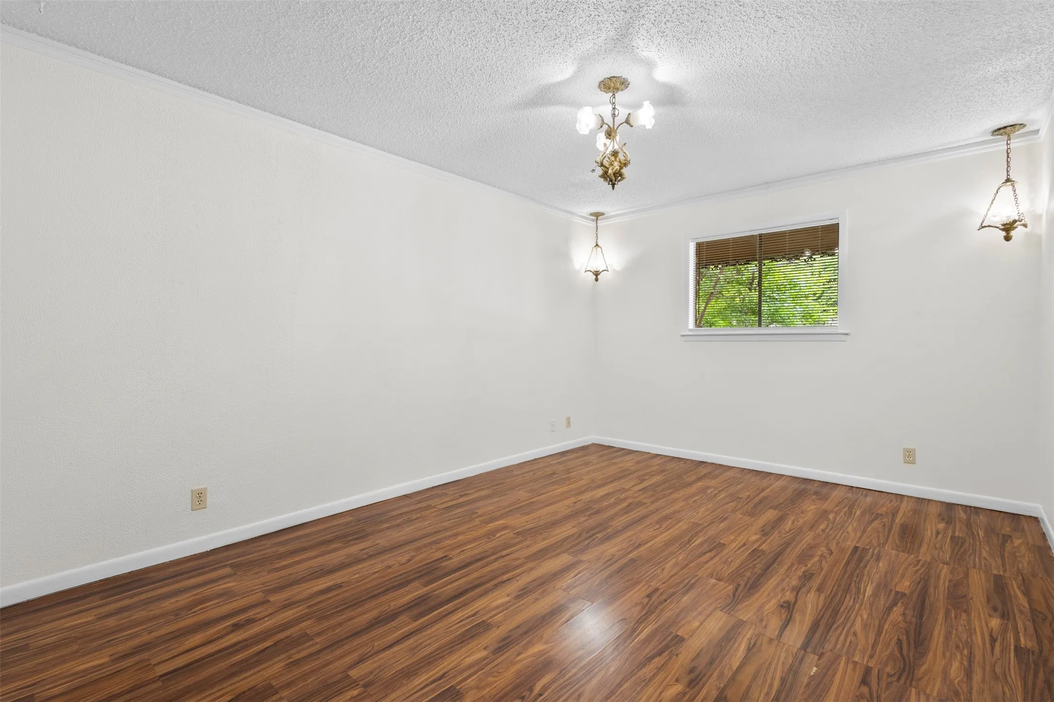 Spare room with dark wood-type flooring, ornamental molding, a textured ceiling, and hanging lights
