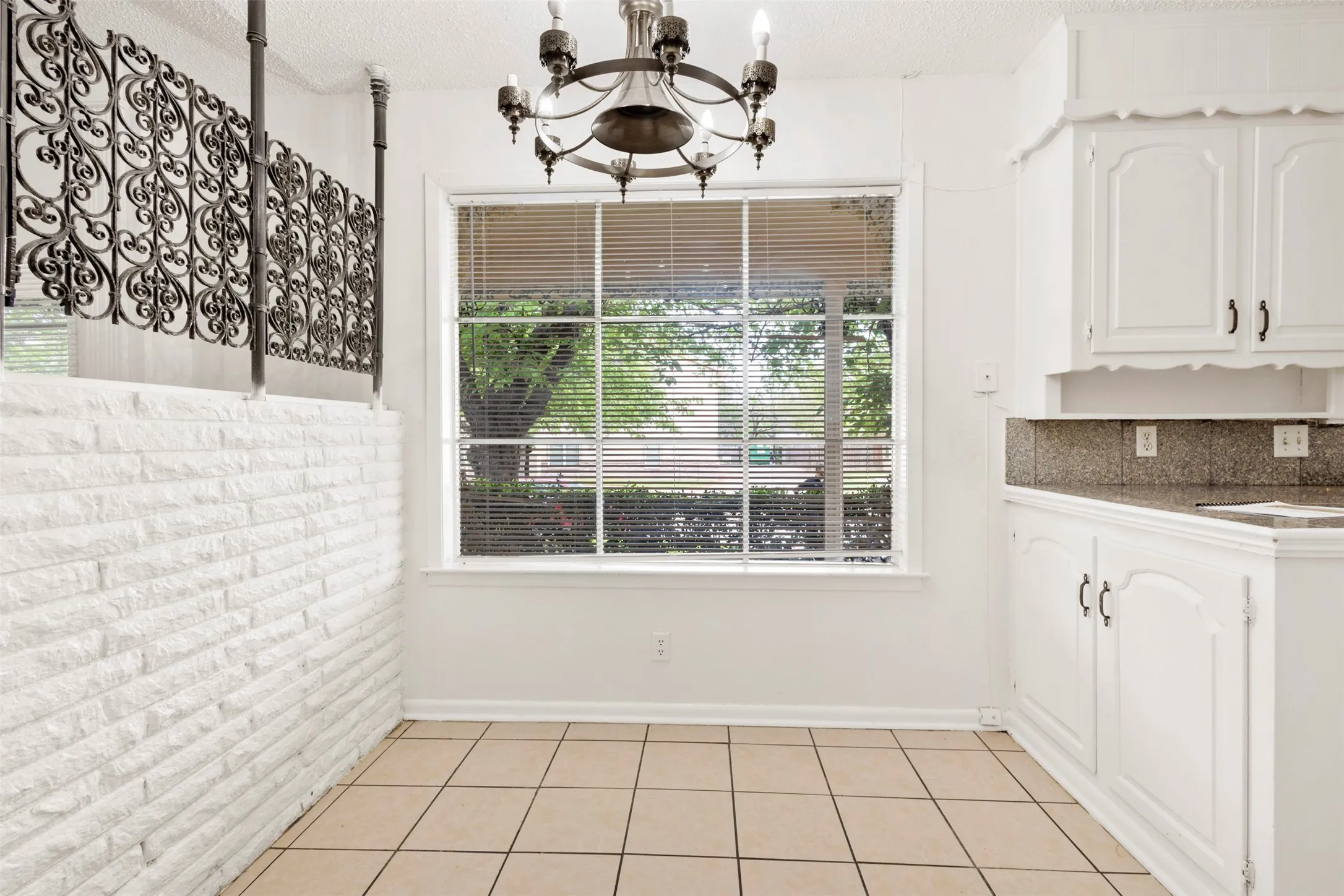 Unfurnished dining area featuring a chandelier, a textured ceiling, light tile patterned flooring, and brick wall