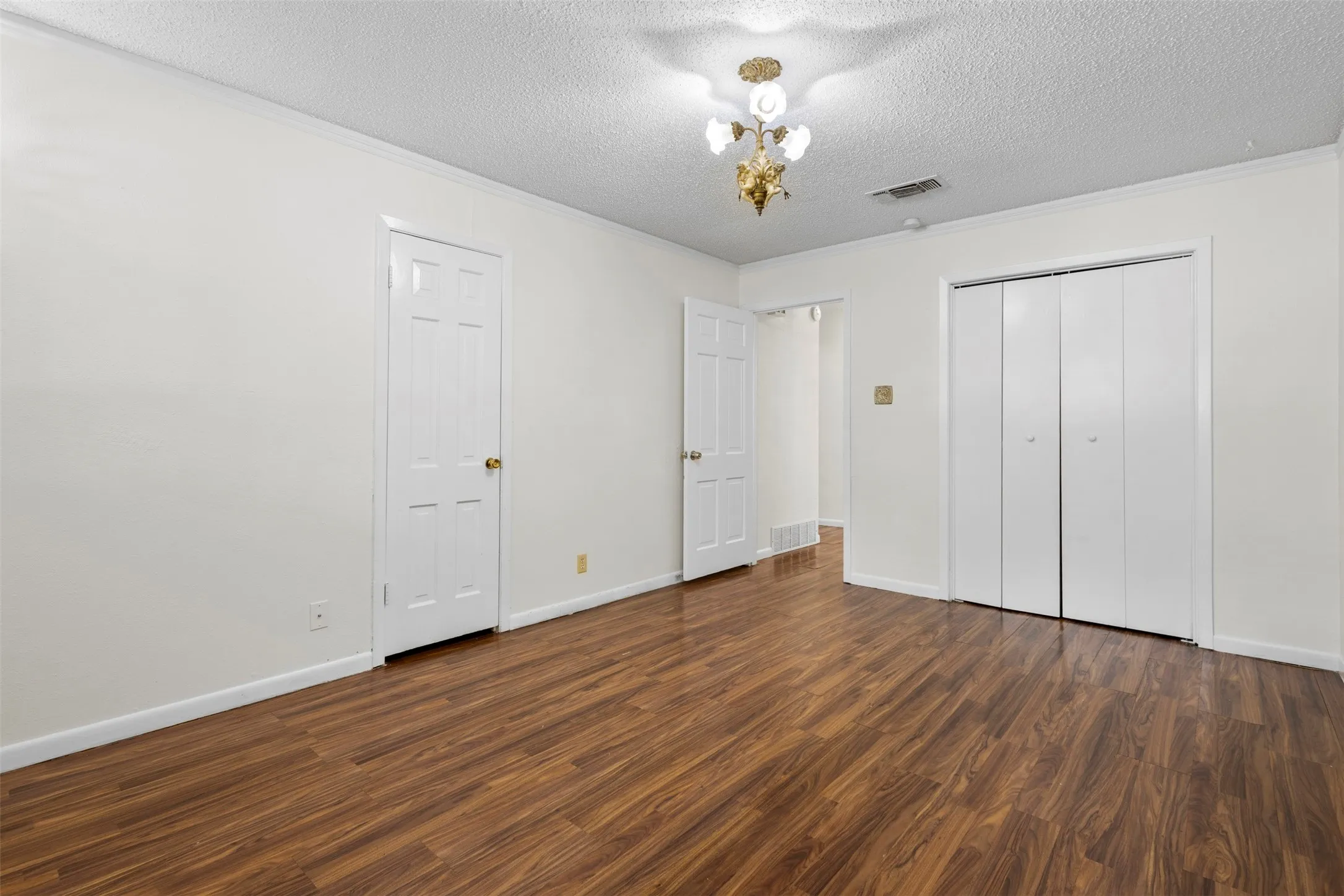Unfurnished bedroom featuring ornamental molding, dark wood-style flooring, and a textured ceiling