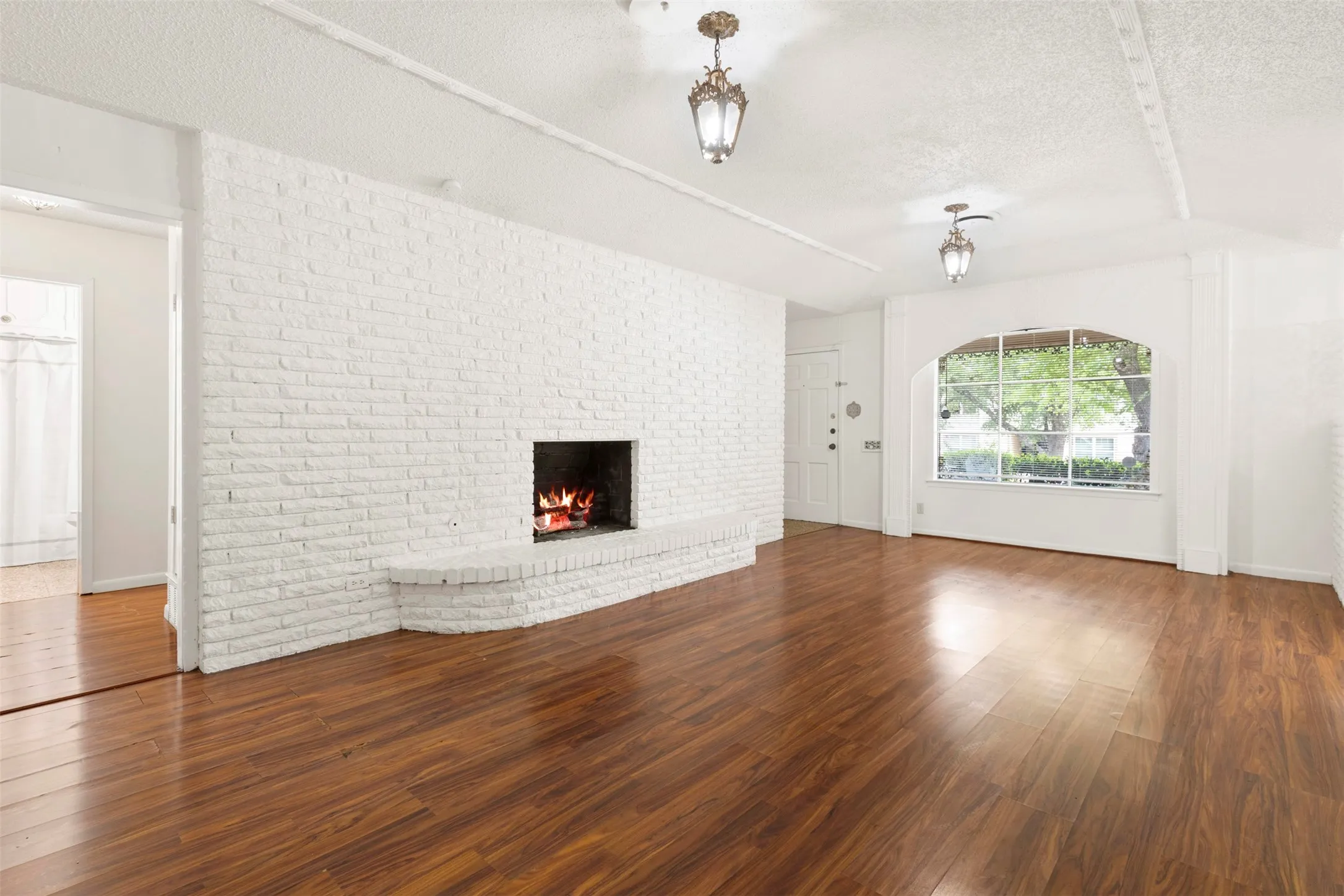 Unfurnished living room featuring a textured ceiling, dark wood finished floors, brick wall, and a brick fireplace