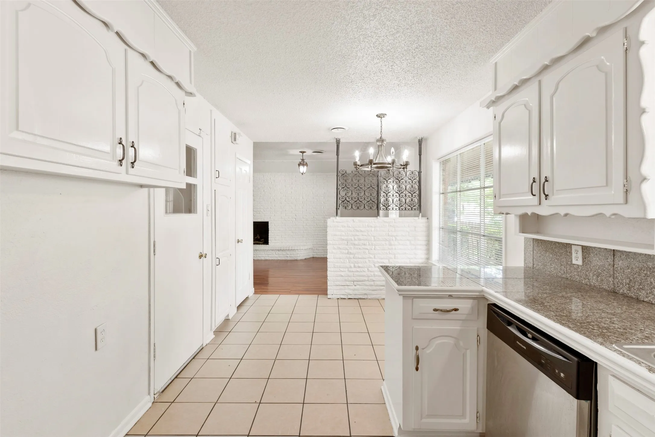 Kitchen with stainless steel dishwasher, white cabinets, a textured ceiling, a chandelier, and tile counters