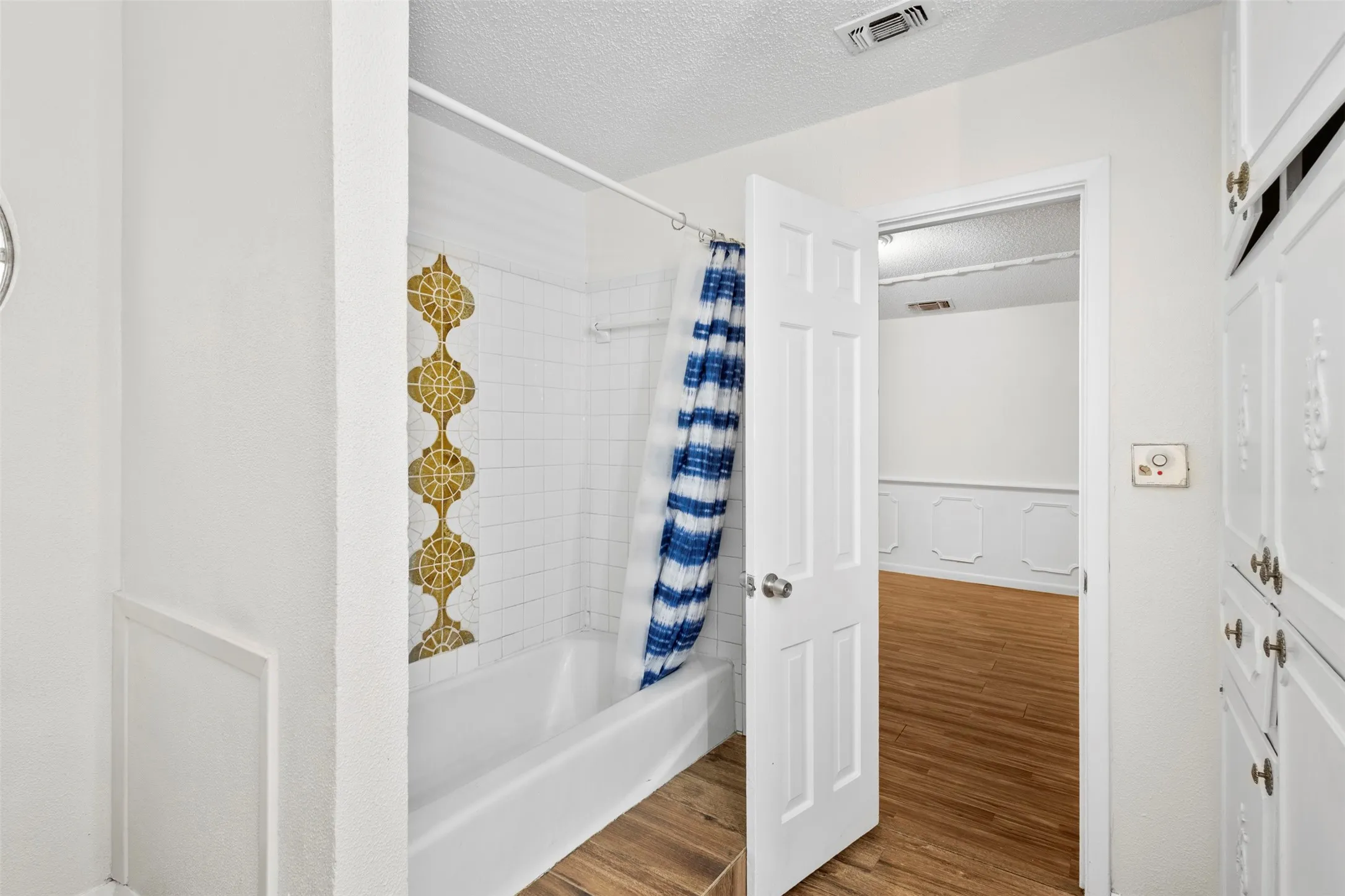 Bathroom with wood finished floors, a textured ceiling, shower / bath combo, and a wainscoted wall