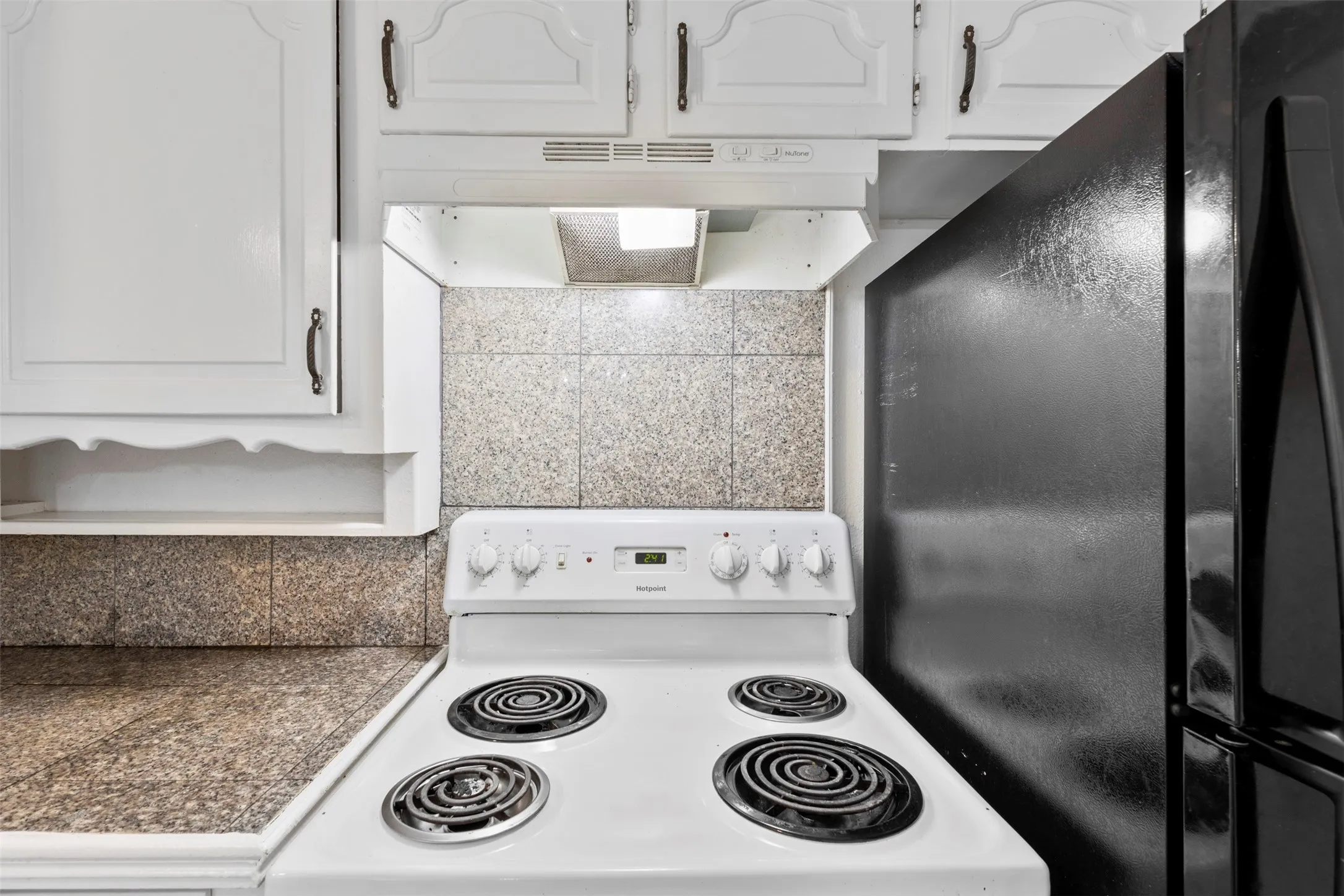 Kitchen with white electric range, white cabinetry, freestanding refrigerator, and tile counters