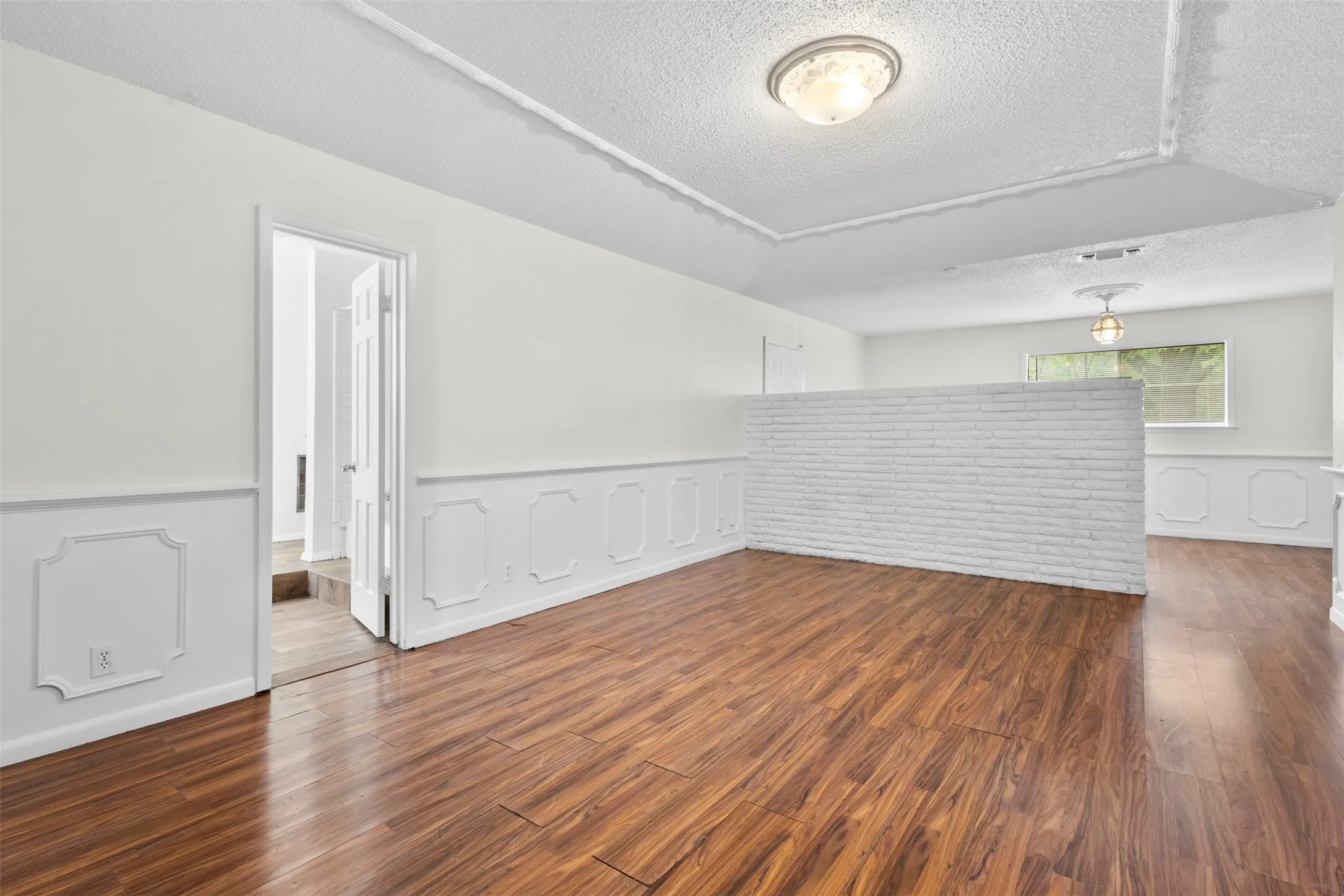 Spare room featuring a wainscoted wall, a decorative wall, dark wood-style floors, and a textured ceiling